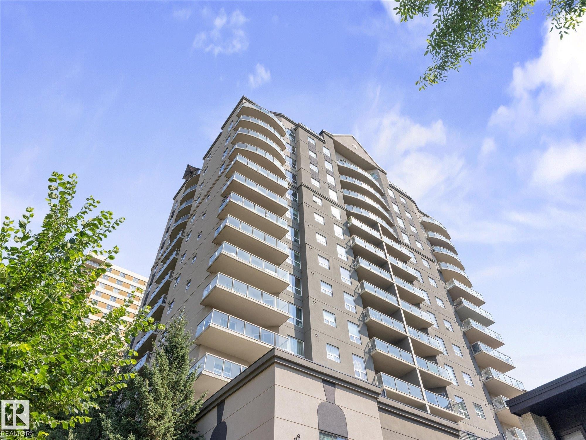 Modern high-rise residential building featuring multiple levels of private balconies with clear glass railings - #707 9819 104 St Nw, Edmonton, AB