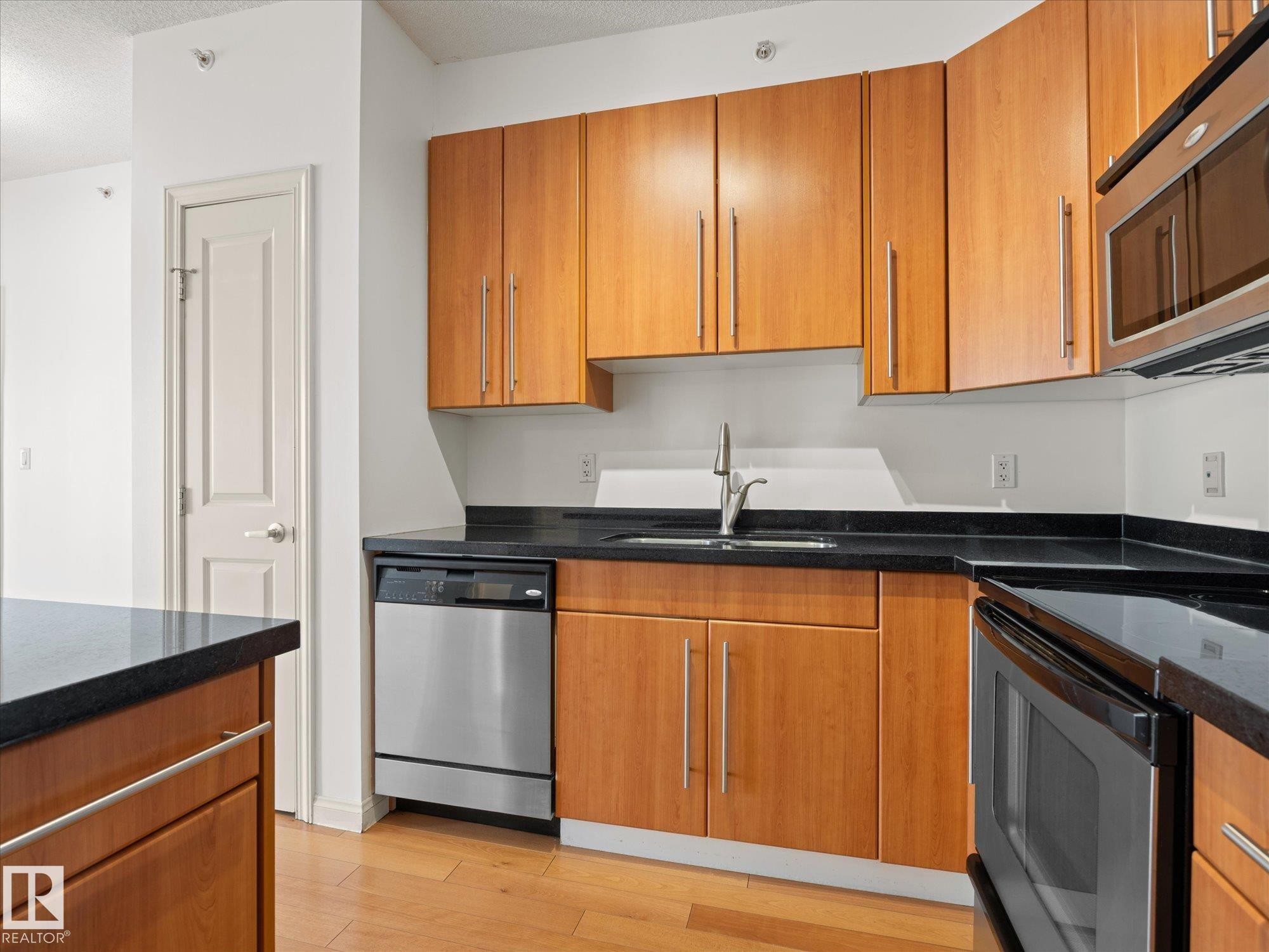 Kitchen featuring wood-finish cabinetry, dark countertops, stainless steel appliances, and wood-finish flooring - #707 9819 104 St Nw, Edmonton, AB