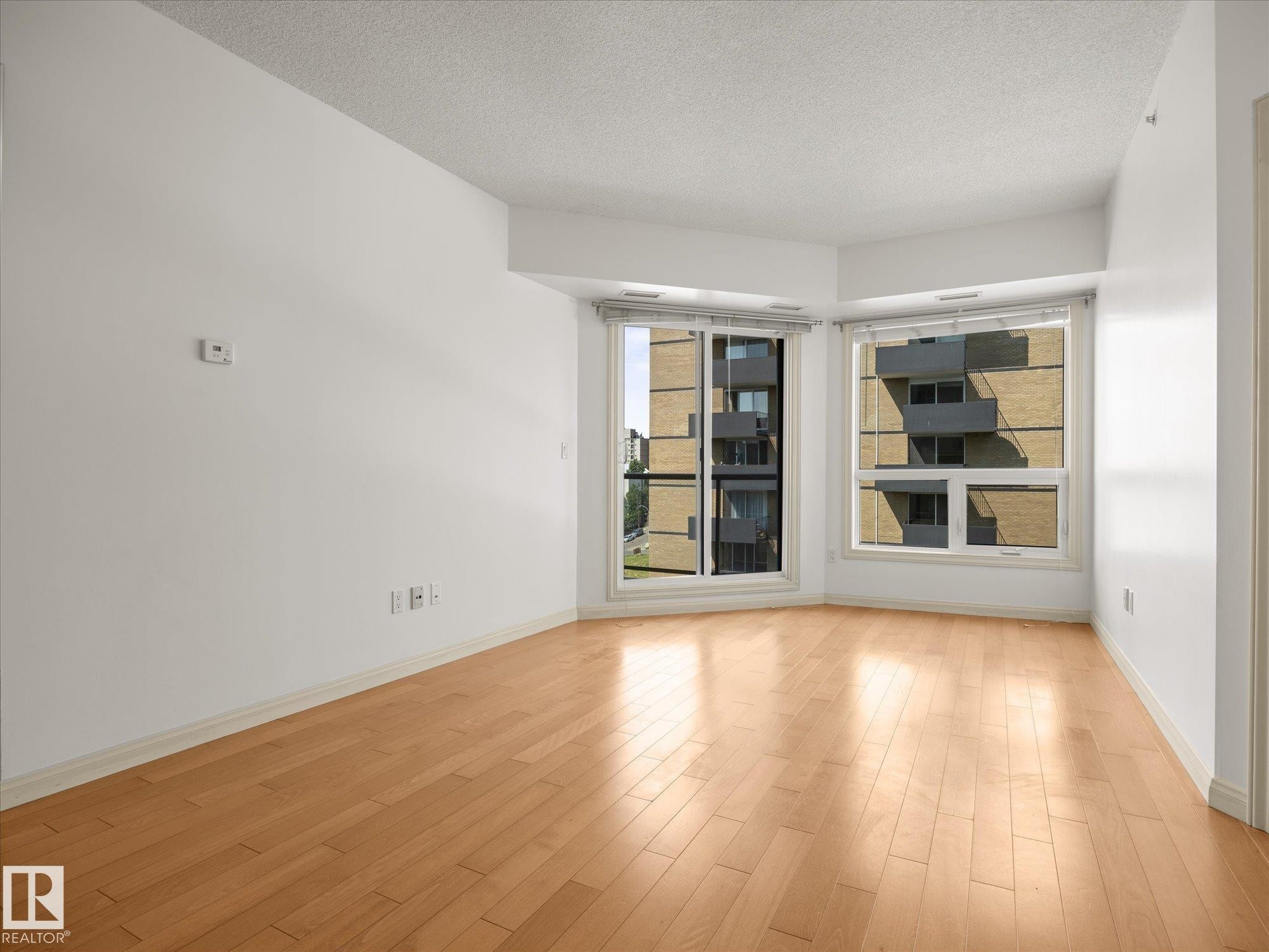 Expansive room featuring light wood-finish flooring, white baseboards, and a neutral wall palette - #707 9819 104 St Nw, Edmonton, AB