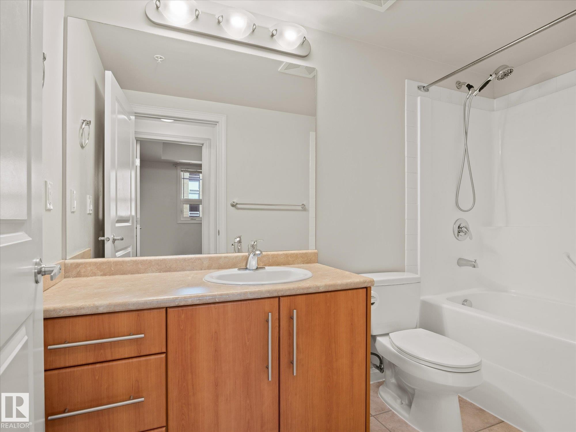 Bathroom featuring a wood-finish vanity with an integrated sink, a light-toned countertop, and a full-width mirror with overhead lighting - #707 9819 104 St Nw, Edmonton, AB