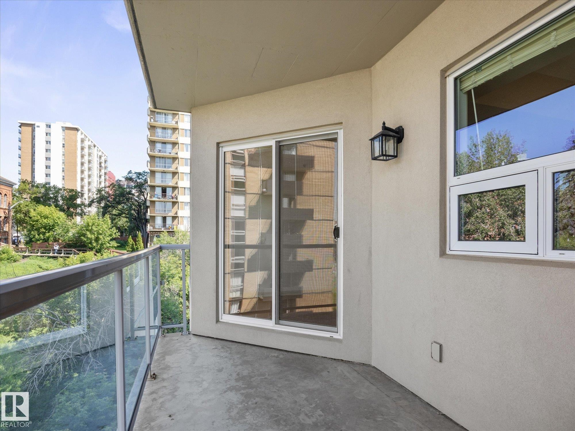 Private outdoor balcony featuring a concrete floor, glass and metal railing, and an exterior wall light fixture - #707 9819 104 St Nw, Edmonton, AB