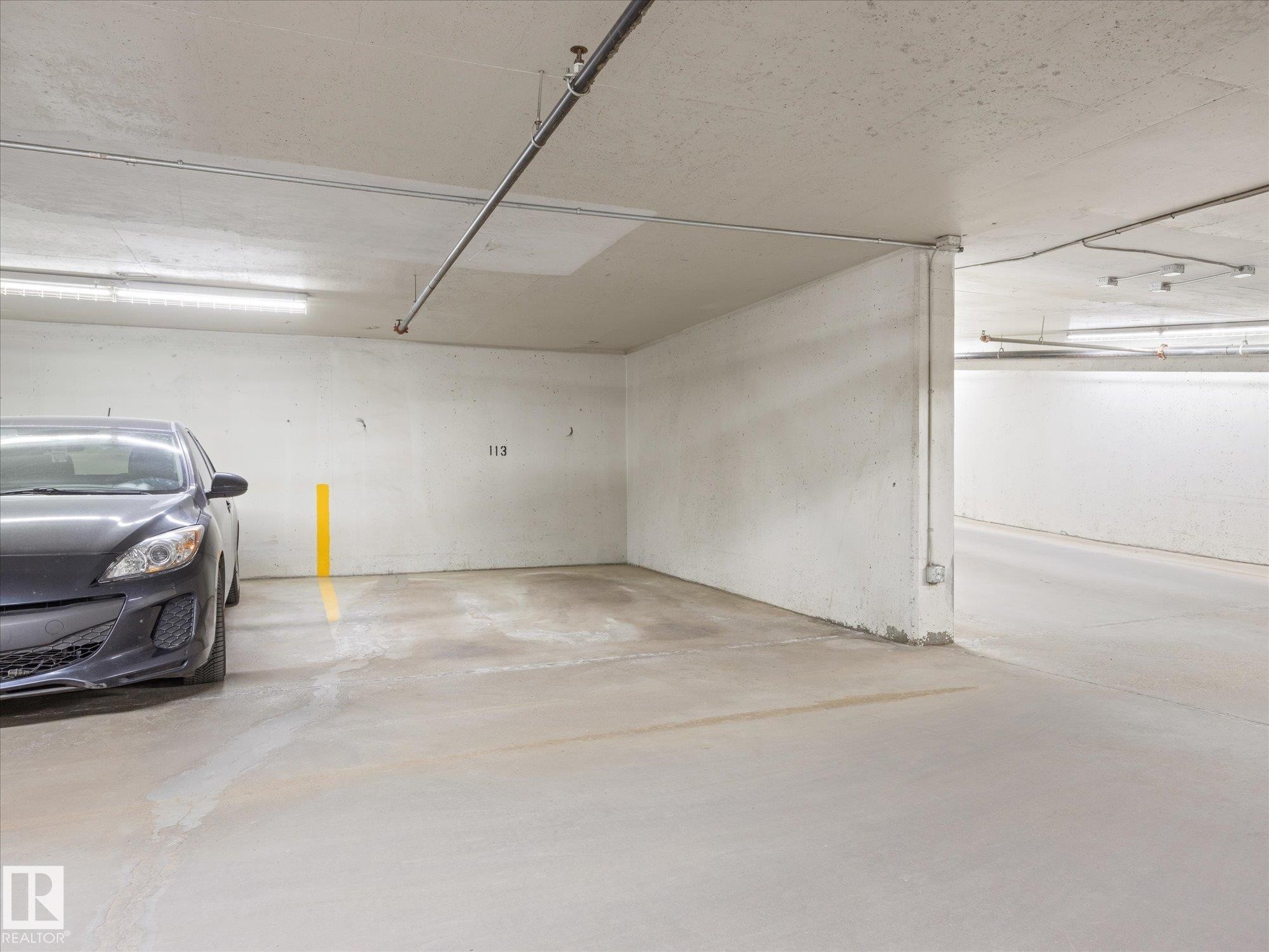 Dedicated parking space featuring concrete flooring, fluorescent overhead lighting, and painted concrete walls - #707 9819 104 St Nw, Edmonton, AB