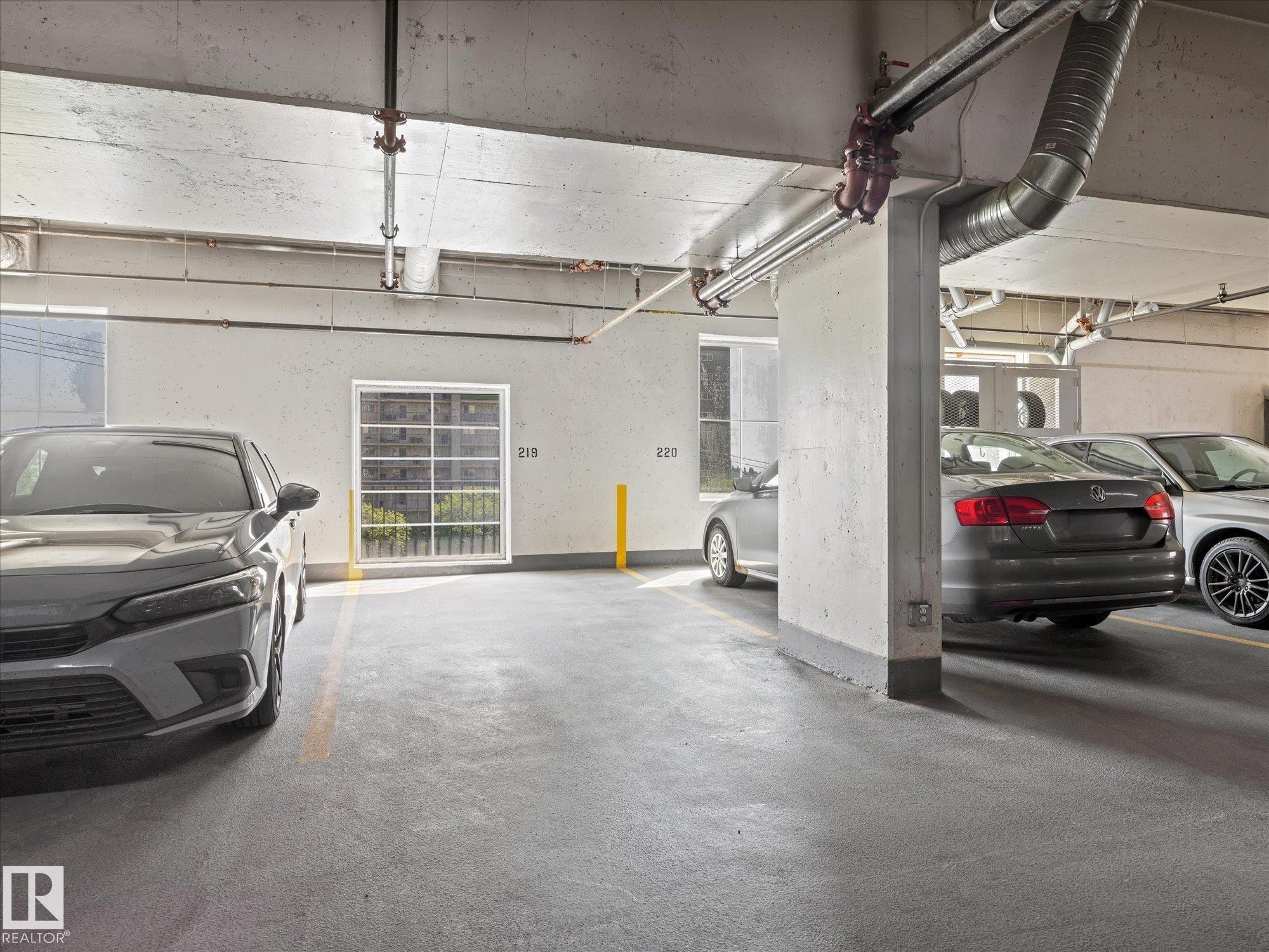 Underground parking garage featuring concrete flooring, exposed ceiling utilities, marked parking spaces, and window access to exterior light - #707 9819 104 St Nw, Edmonton, AB