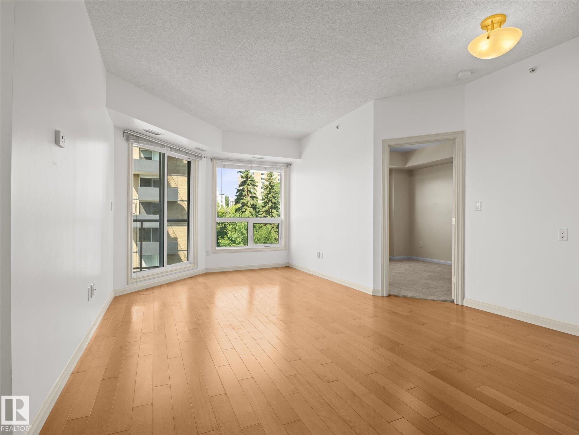 Open-concept room featuring wood-finish flooring, white walls, and a recessed window bay with multiple windows - #707 9819 104 St Nw, Edmonton, AB