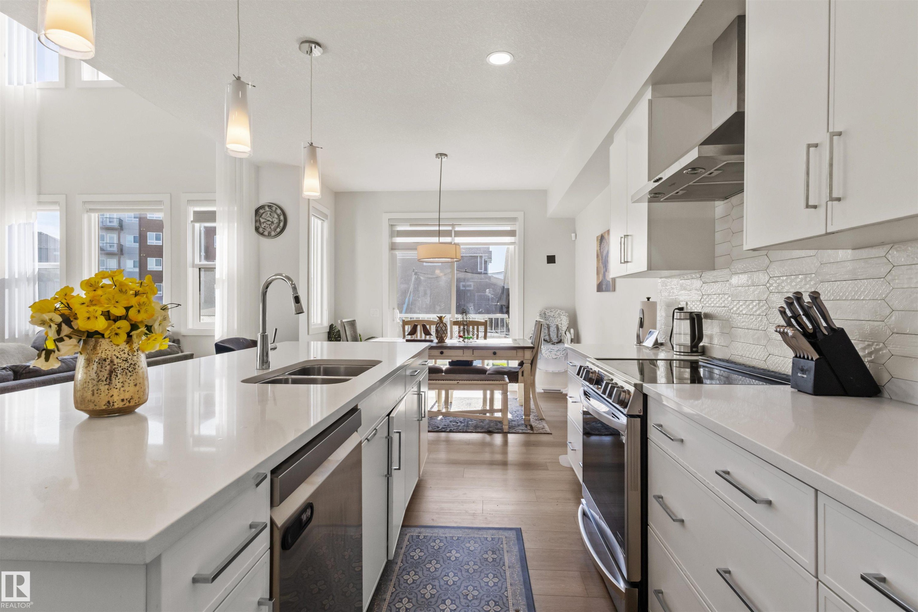 Modern kitchen featuring an expansive island with an undermount sink, stainless steel appliances, white cabinetry with contemporary hardware, a decorative tile backsplash, and wood-finish flooring - 1471 Plum Circle Sw, Edmonton, AB - Indoor Photo Showing Kitchen With Double Sink With Upgraded Kitchen