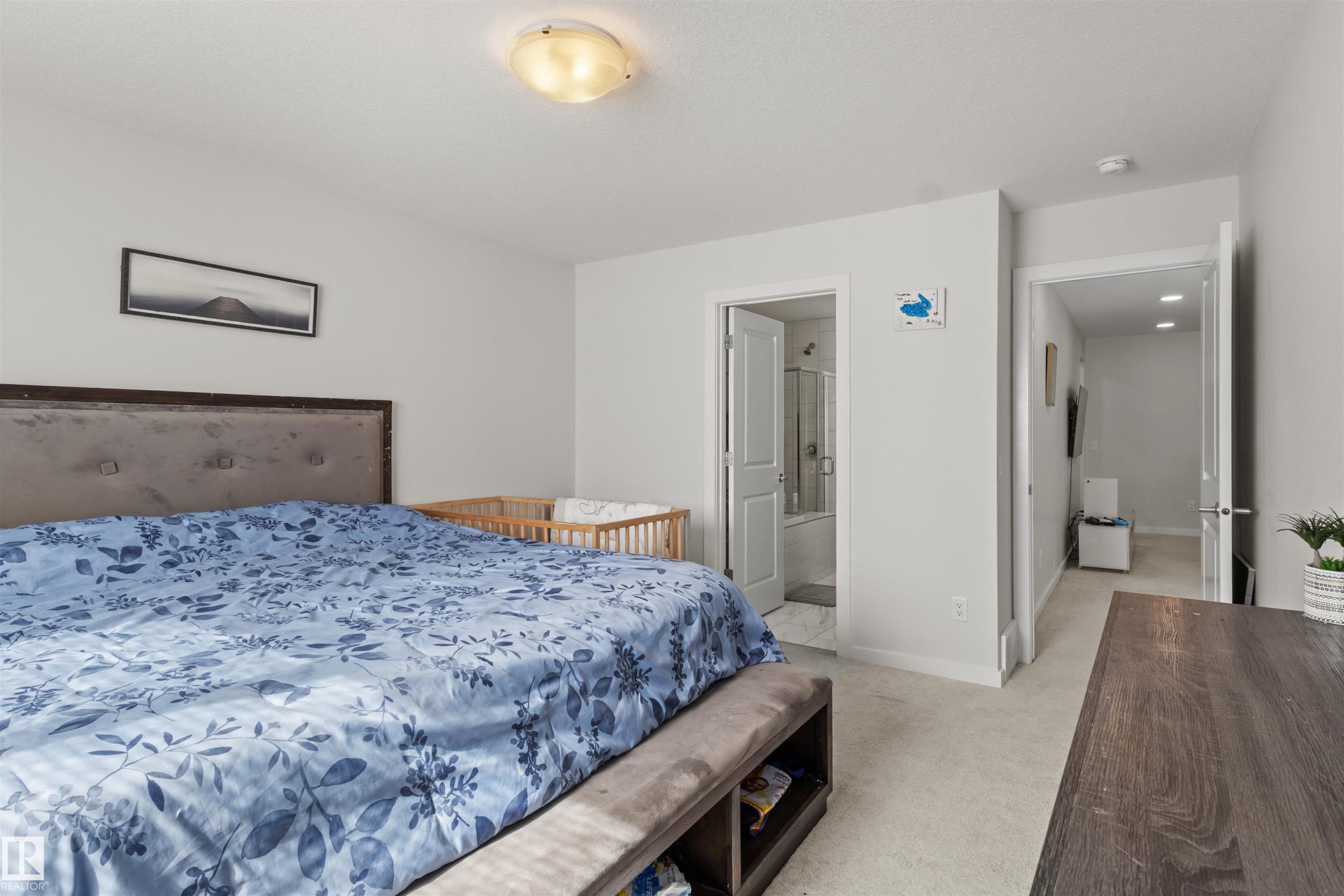 Carpeted bedroom featuring light gray walls, a built-in light fixture, and an open doorway revealing a bathroom with a shower-tub combination - 1471 Plum Circle Sw, Edmonton, AB - Indoor Photo Showing Bedroom