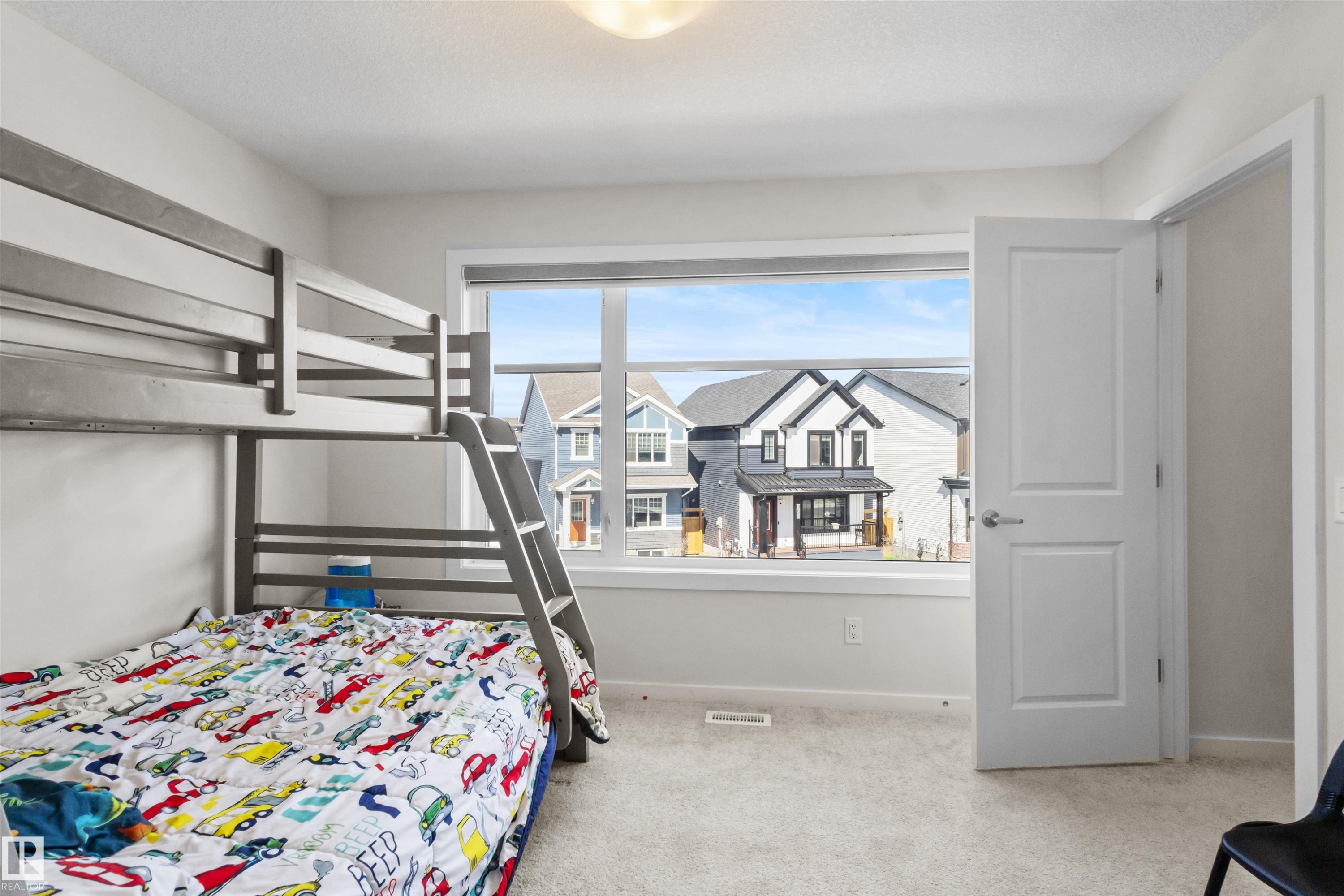 Bedroom featuring light gray carpeting, a large window with white trim, and a white interior door with a silver handle - 1471 Plum Circle Sw, Edmonton, AB - Indoor Photo Showing Bedroom