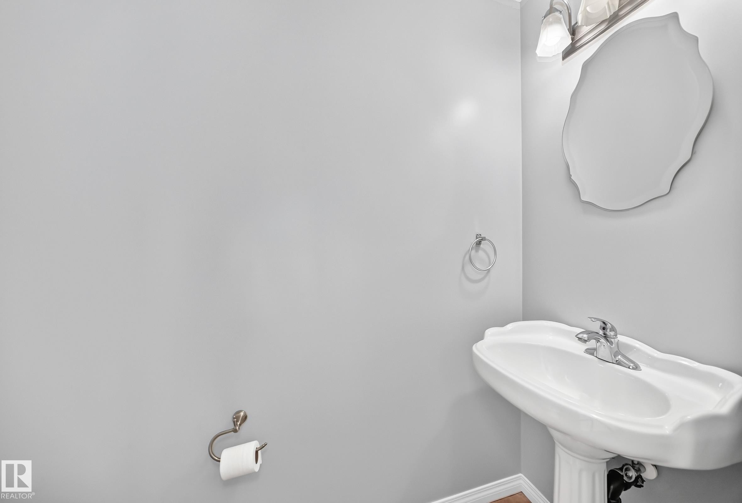 Pedestal sink with chrome faucet, complemented by a decorative wall mirror and a three-light vanity fixture - 9333 103A Avenue Nw, Edmonton, AB - Indoor Photo Showing Bathroom