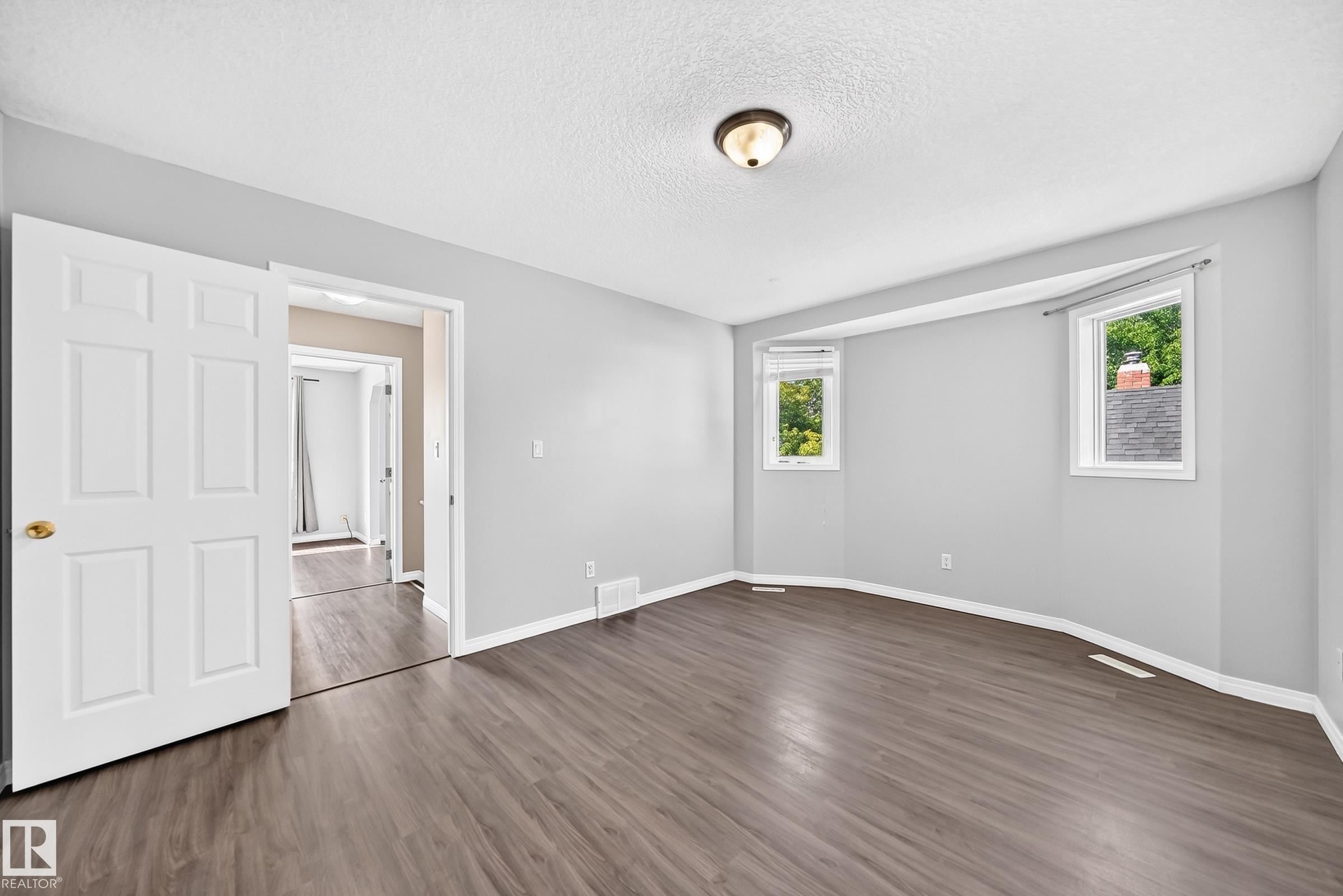 Spacious room featuring wood-finish flooring, light grey walls, and a multi-panel interior door - 9333 103A Avenue Nw, Edmonton, AB - Indoor Photo Showing Other Room