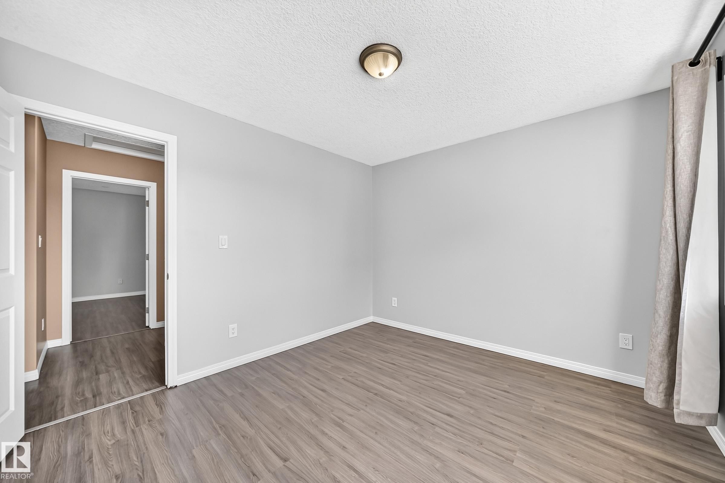 Room featuring wood-finish flooring, light gray wall paint, white baseboards, and a bronze-finish ceiling light fixture - 9333 103A Avenue Nw, Edmonton, AB - Indoor Photo Showing Other Room