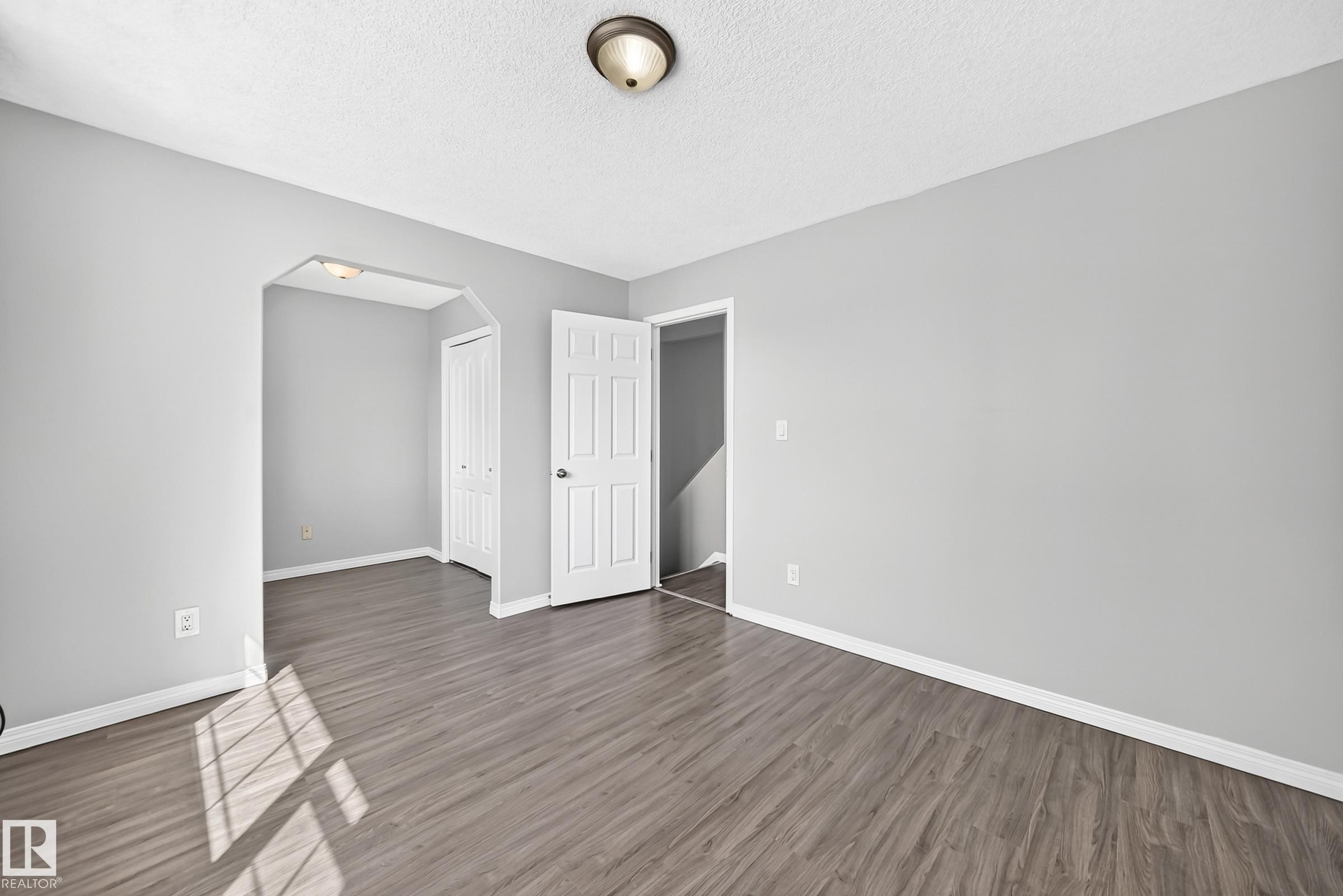 Spacious room featuring wood-finish flooring, light grey walls, white baseboards, a white paneled door, and a flush mount ceiling light - 9333 103A Avenue Nw, Edmonton, AB - Indoor Photo Showing Other Room