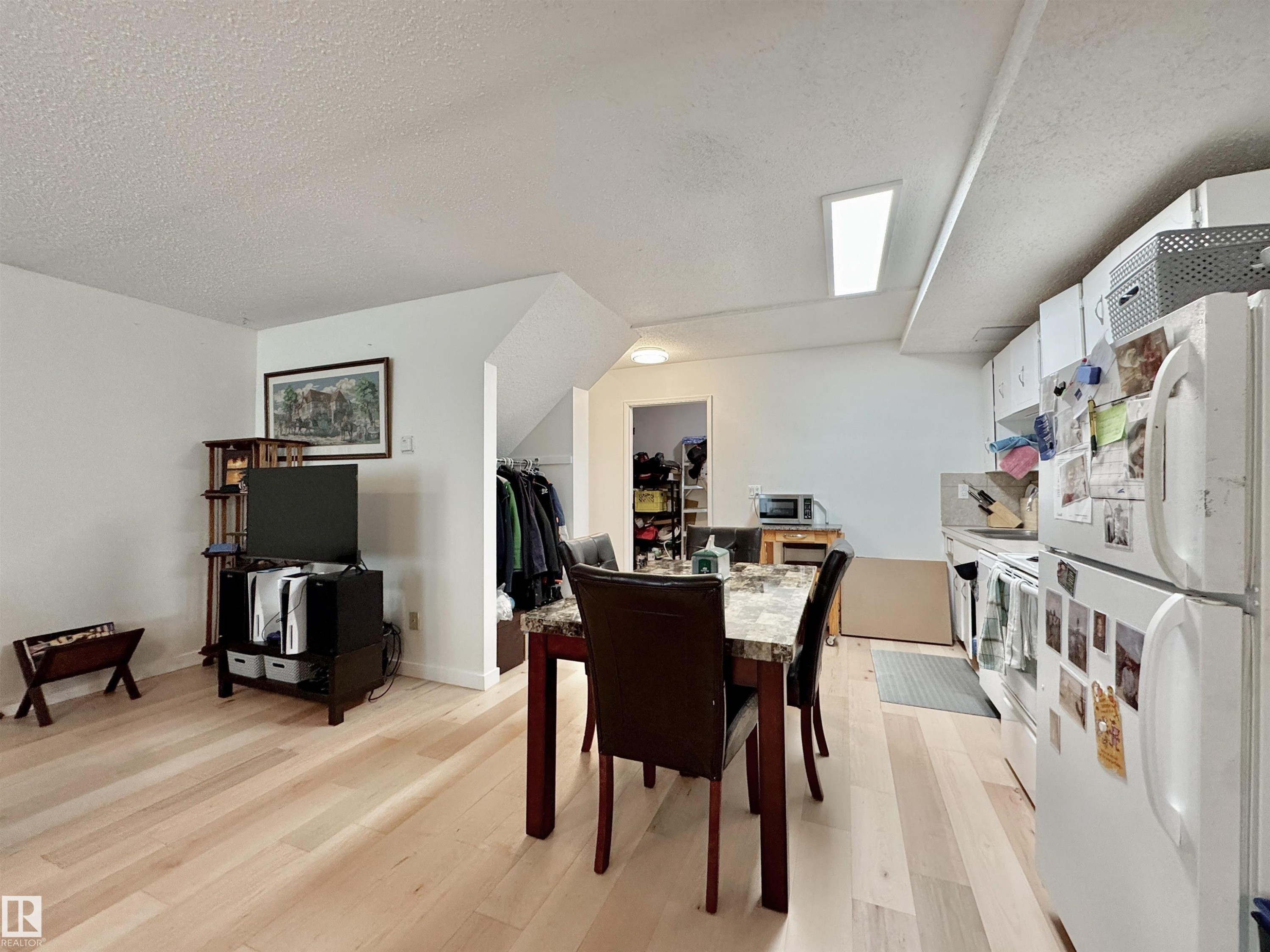 Open-concept living space featuring light wood-finish flooring, white cabinetry, and a dining area with a stone-finish table - #29 13580 38 St Nw, Edmonton, AB - Indoor Photo Showing Dining Room
