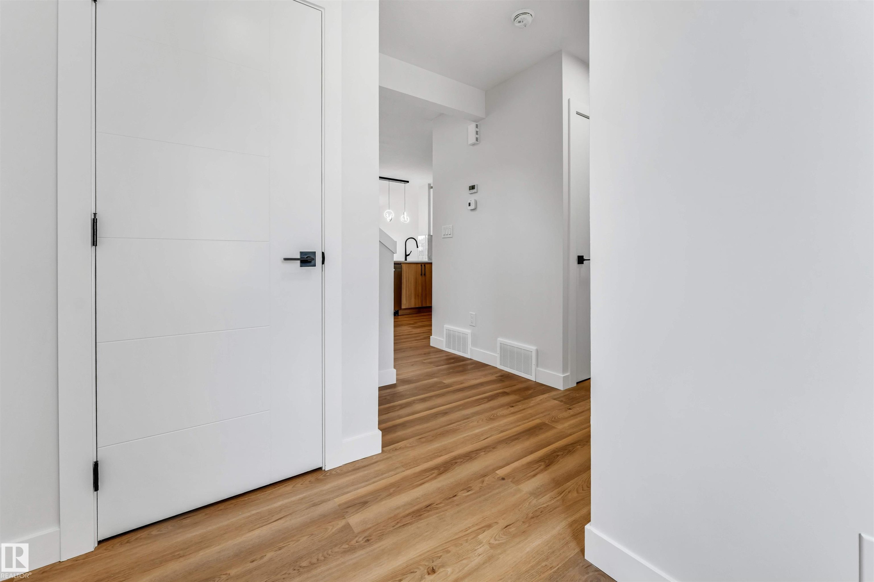 Interior hallway featuring wood-finish flooring, white walls, and modern white doors with matte black hardware - 1712 27 St Nw, Edmonton, AB - Indoor Photo Showing Other Room