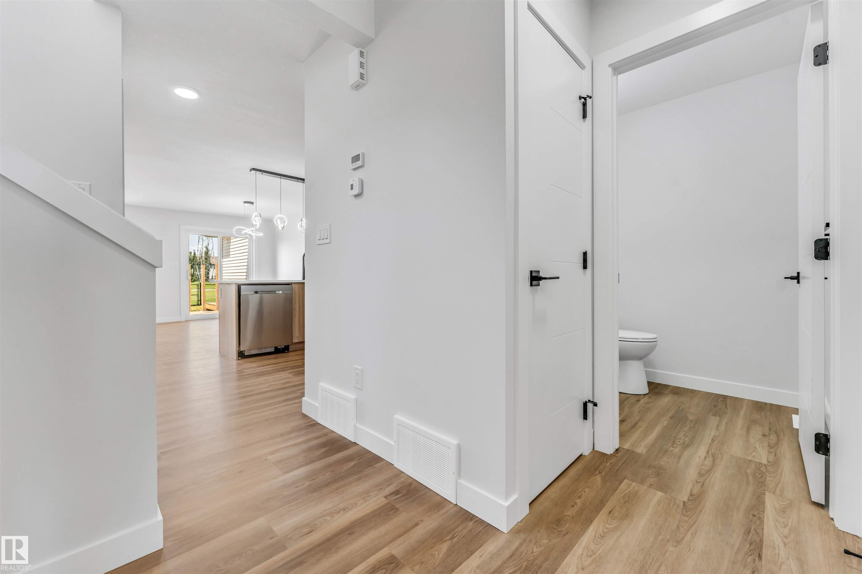 Bright hallway featuring wood-finish flooring, white trim, and a white interior door with matte black hardware - 1712 27 St Nw, Edmonton, AB - Indoor Photo Showing Other Room