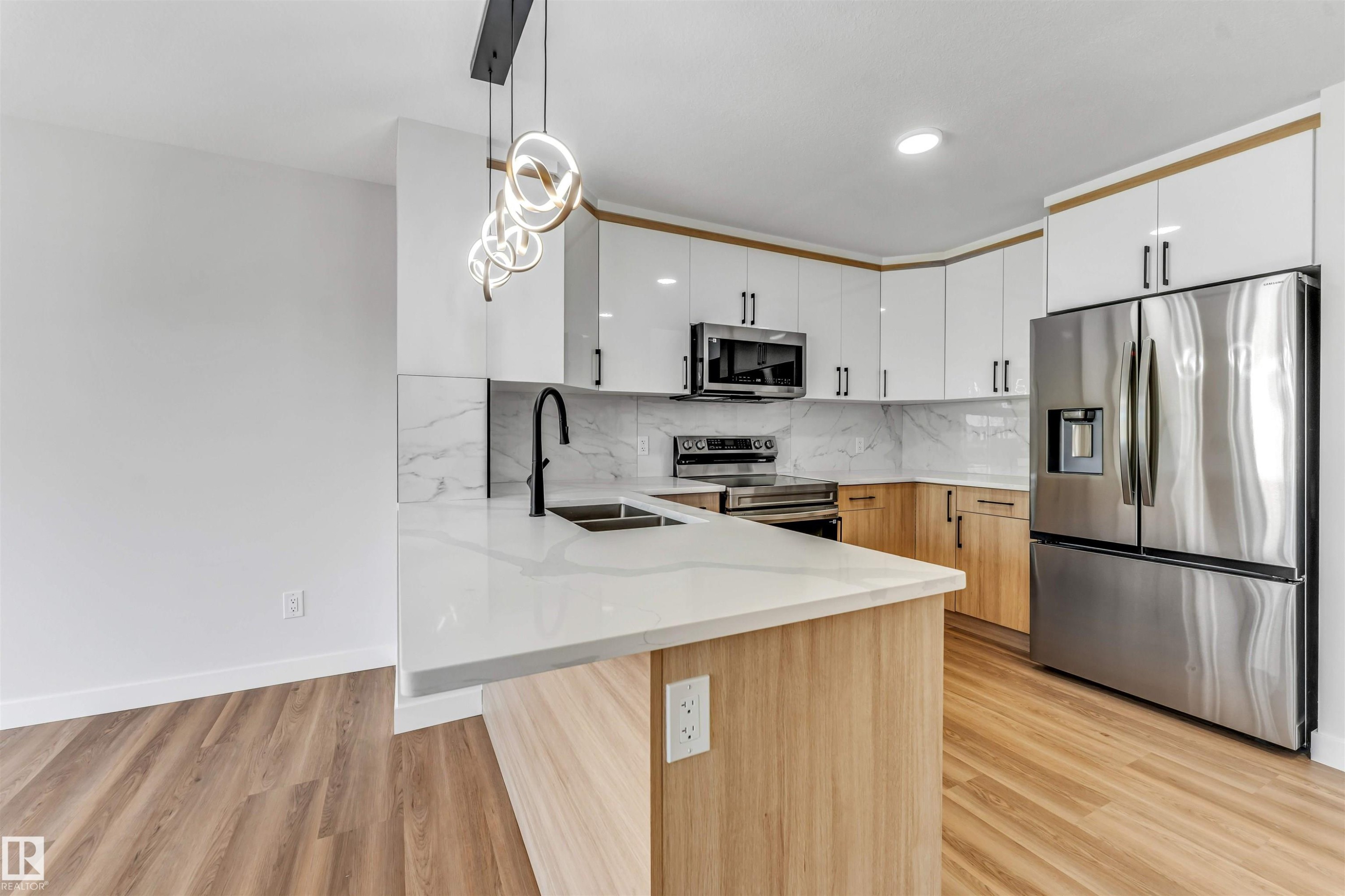 Modern kitchen featuring white and natural wood-finish cabinetry, stainless steel appliances, a white countertop island with an integrated sink, a sleek black faucet, and wood-finish flooring - 1712 27 St Nw, Edmonton, AB - Indoor Photo Showing Kitchen With Double Sink With Upgraded Kitchen