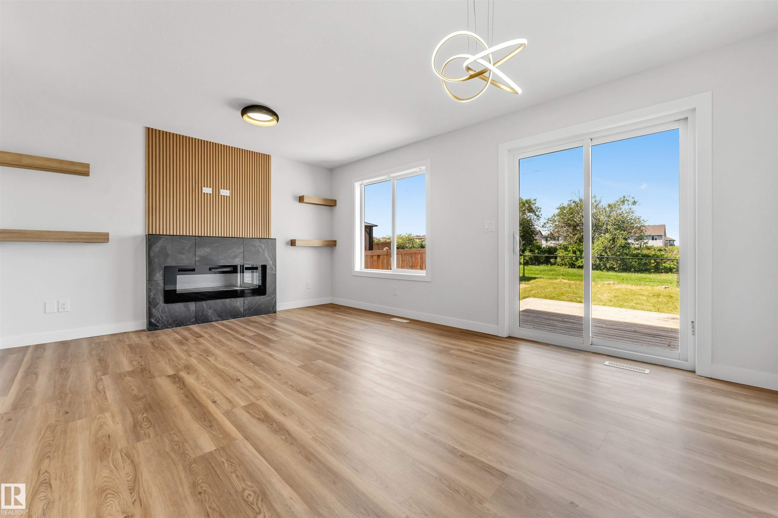 Spacious room featuring wood-finish flooring, a contemporary fireplace with a dark stone surround and wood slat accent wall, and a modern ceiling light fixture - 1712 27 St Nw, Edmonton, AB - Indoor Photo Showing Living Room With Fireplace