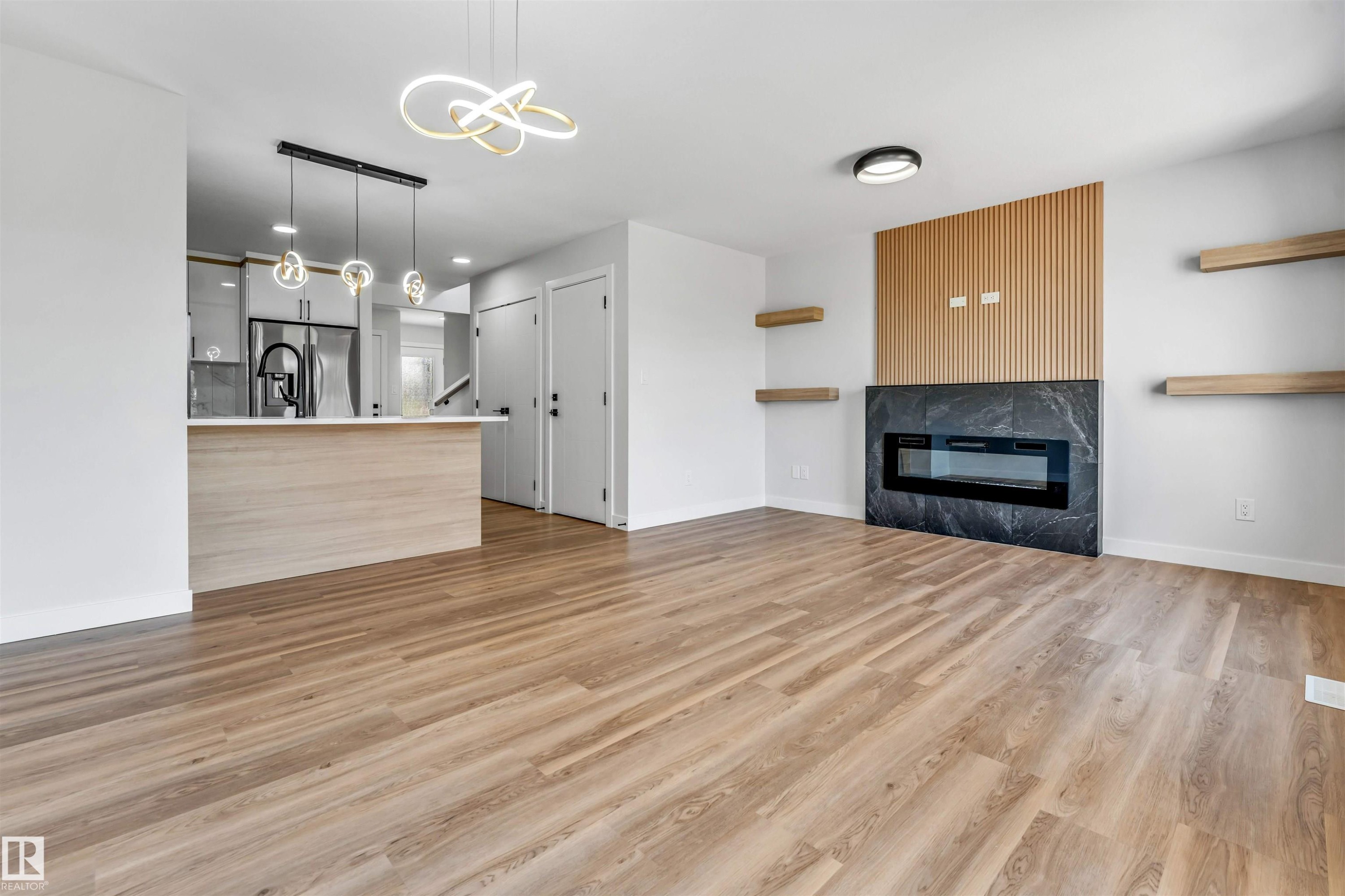 Open-concept living space featuring wood-finish flooring, a contemporary fireplace with a dark stone surround, and a slatted wood accent wall - 1712 27 St Nw, Edmonton, AB - Indoor Photo Showing Other Room With Fireplace