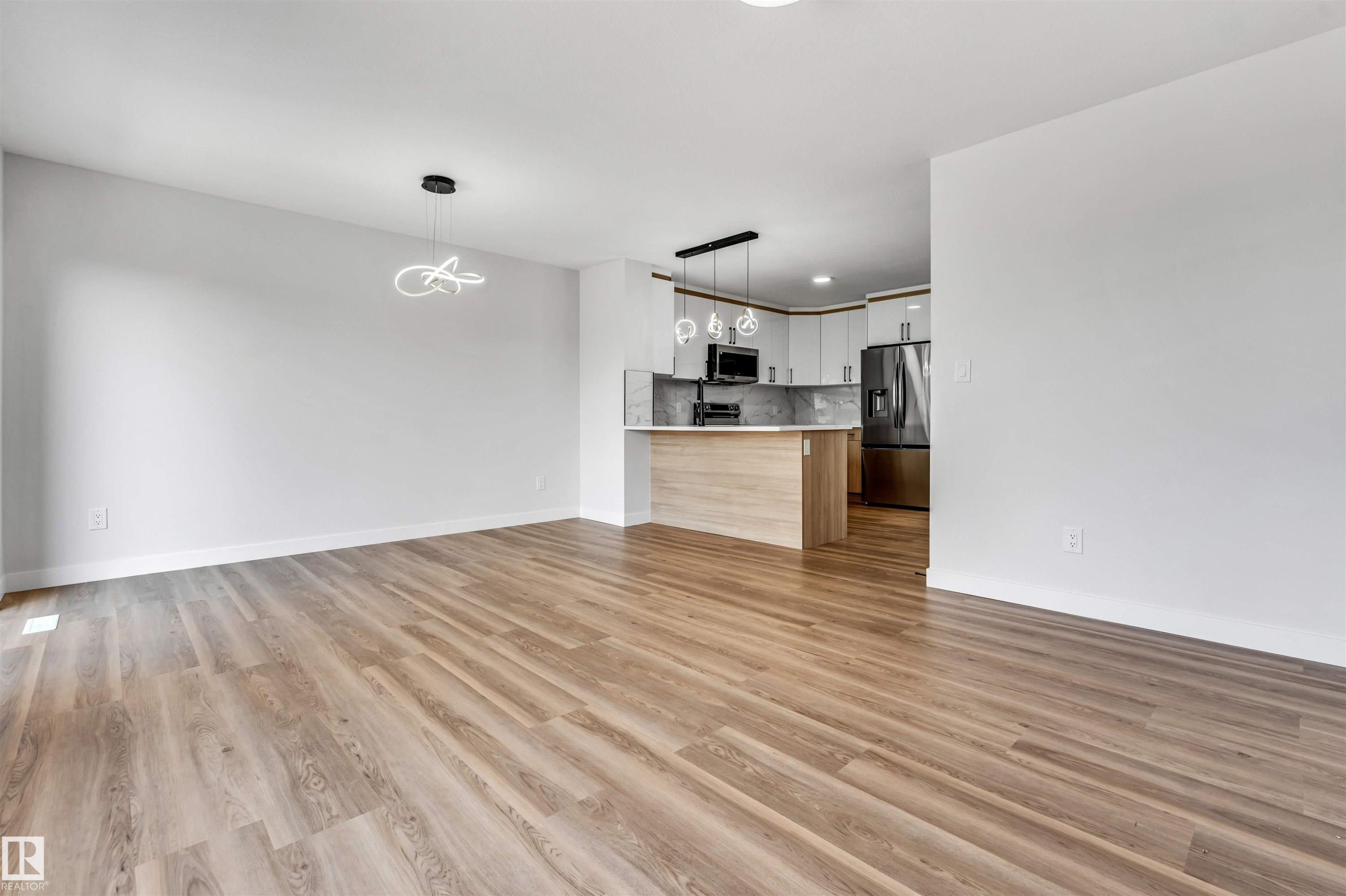 Bright, open-concept living space featuring wood-finish flooring, a modern linear pendant light fixture, and recessed lighting - 1712 27 St Nw, Edmonton, AB - Indoor Photo Showing Kitchen