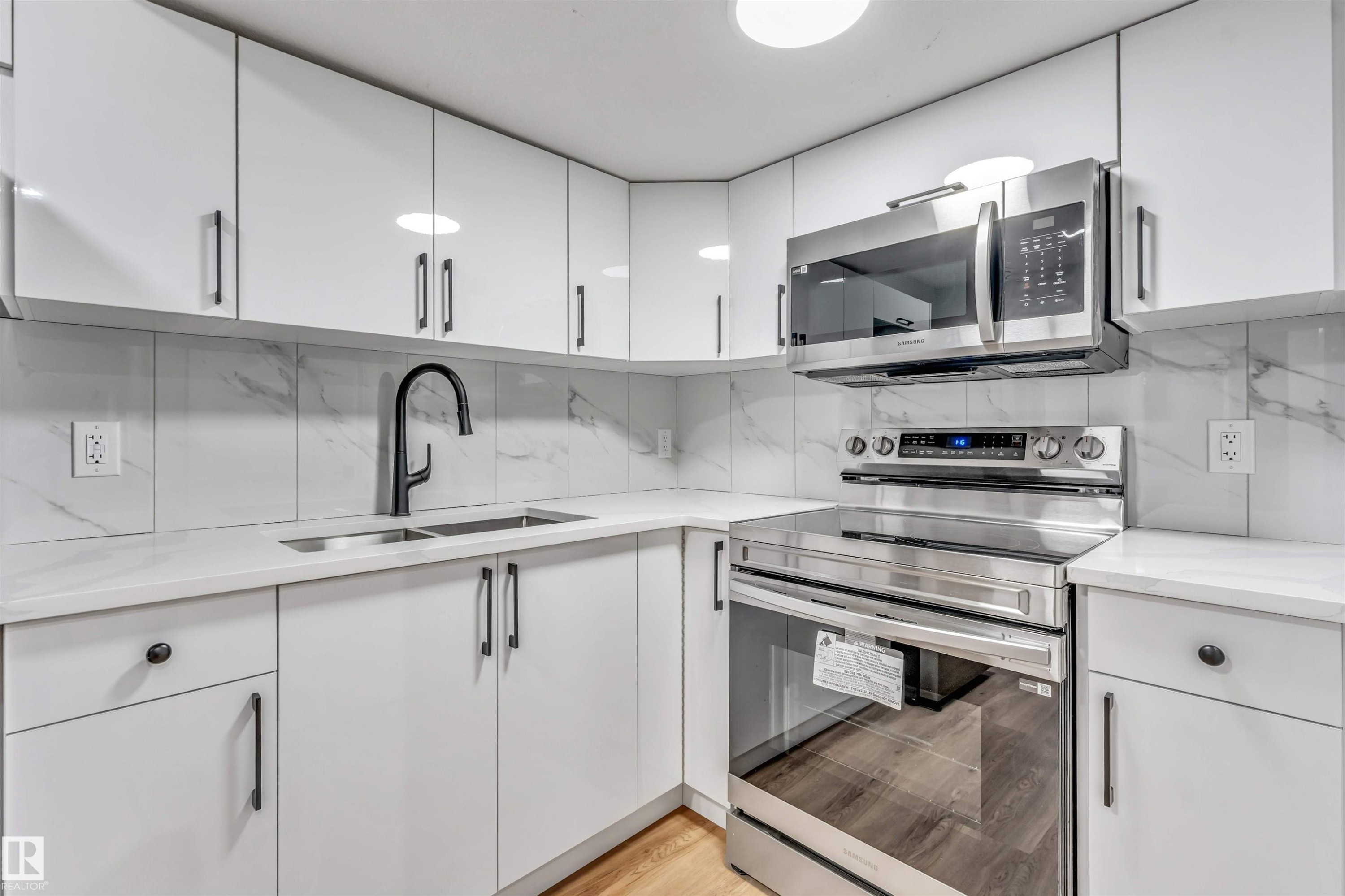 Kitchen featuring white cabinetry, light-toned countertops, a matte black gooseneck faucet, a stainless steel range, and an over-the-range microwave - 1712 27 St Nw, Edmonton, AB - Indoor Photo Showing Kitchen With Double Sink