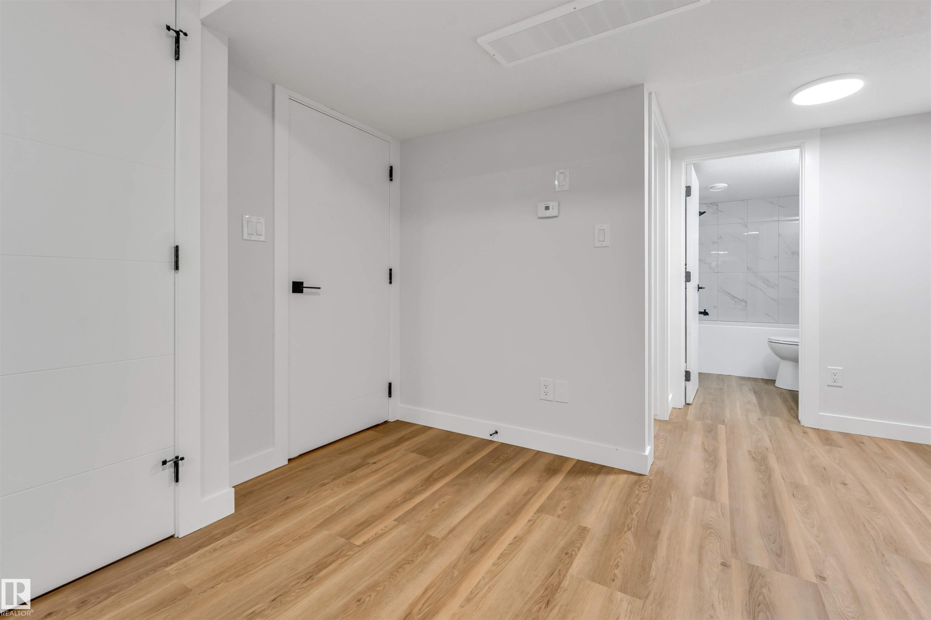 Interior space featuring wood-finish flooring, white walls, and contemporary black hardware on white doors - 1712 27 St Nw, Edmonton, AB - Indoor Photo Showing Other Room