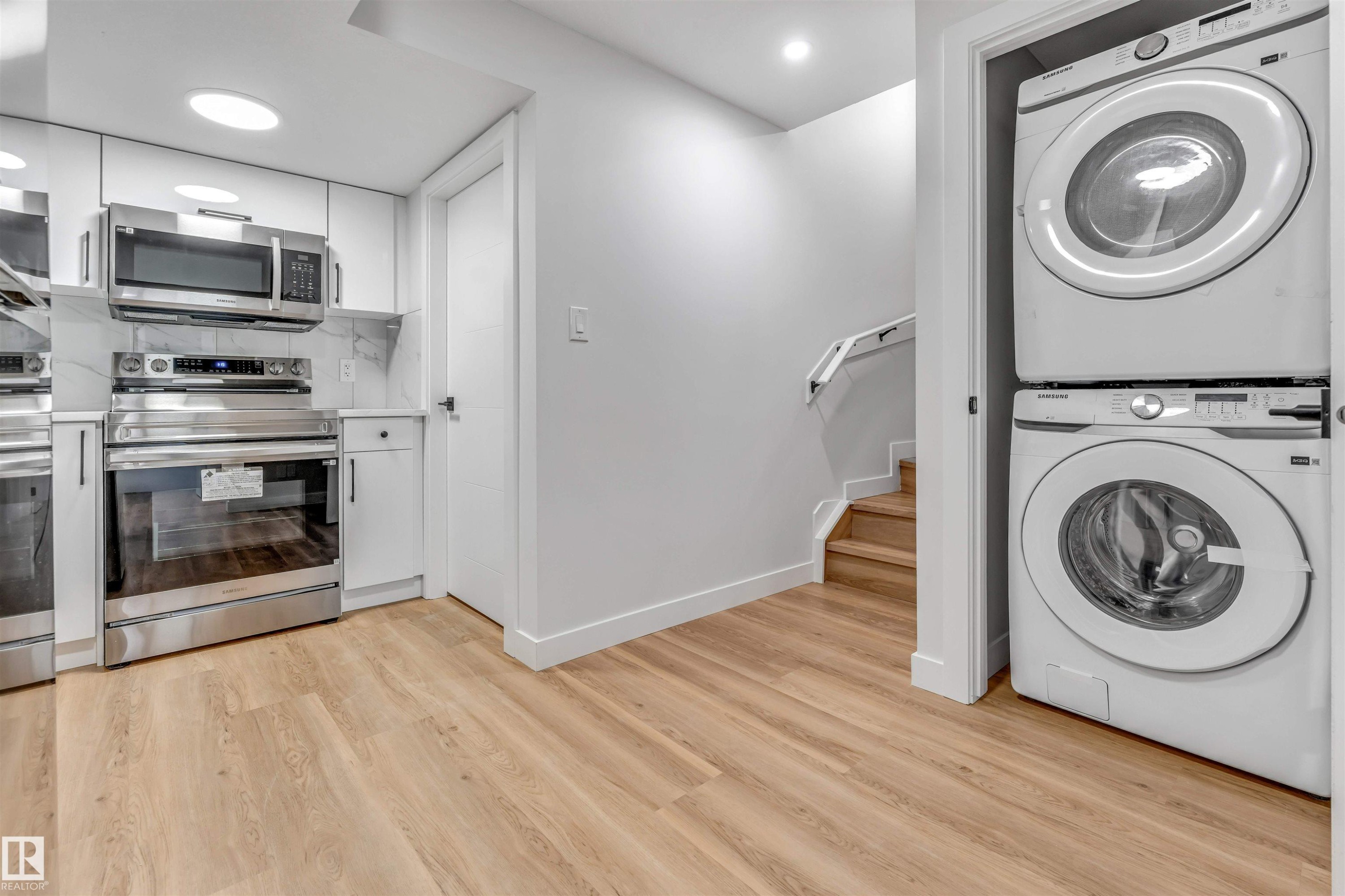 Kitchenette featuring stainless steel appliances, white cabinetry, and wood-finish flooring - 1712 27 St Nw, Edmonton, AB - Indoor Photo Showing Laundry Room