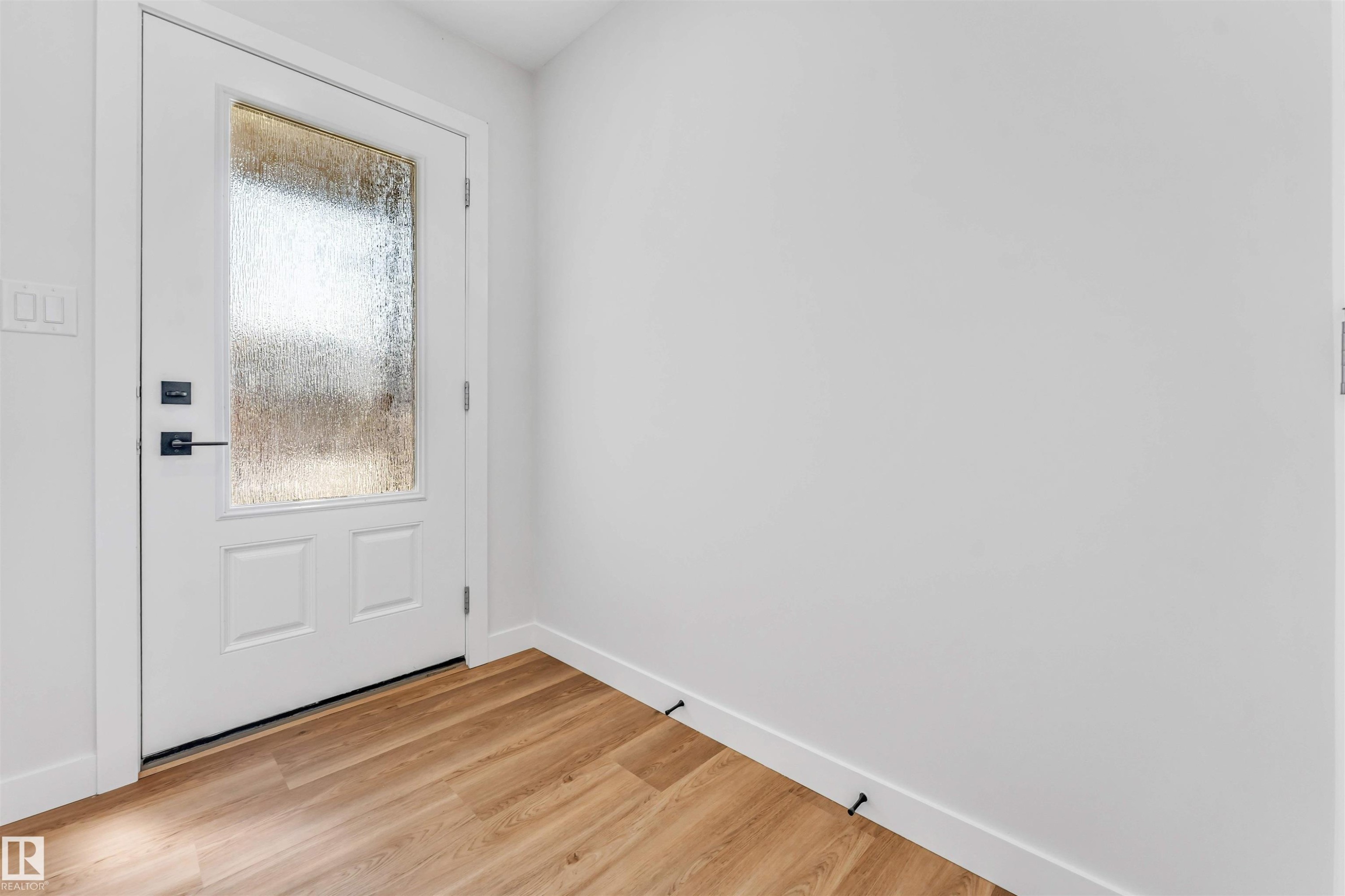 White panel door with frosted glass insert, matte black hardware, and wood-finish flooring - 1712 27 St Nw, Edmonton, AB - Indoor Photo Showing Other Room