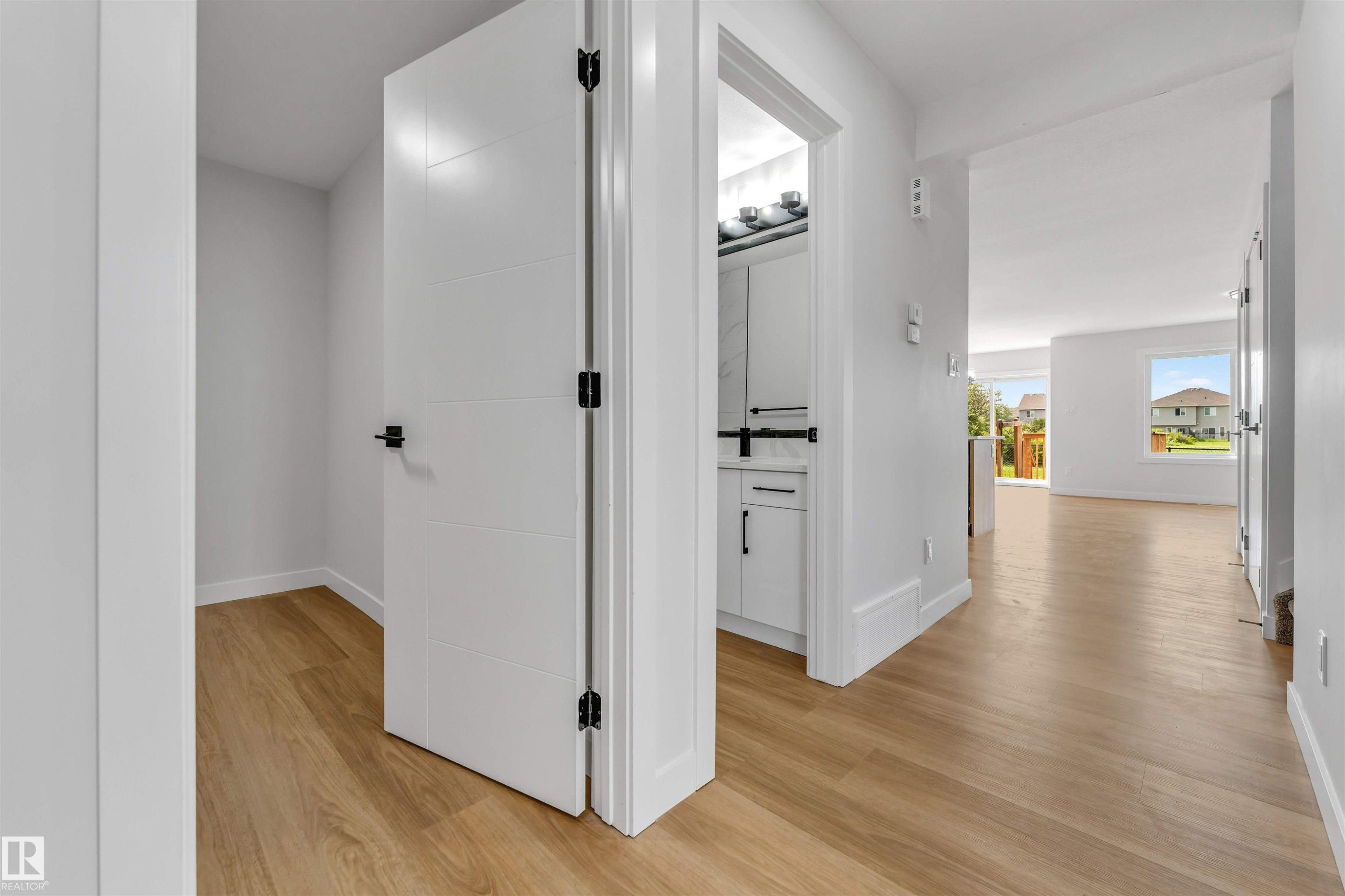 Light wood-finish flooring throughout, modern white interior doors with matte black hardware, and crisp white trim - 1714 27 St. Nw, Edmonton, AB - Indoor Photo Showing Other Room