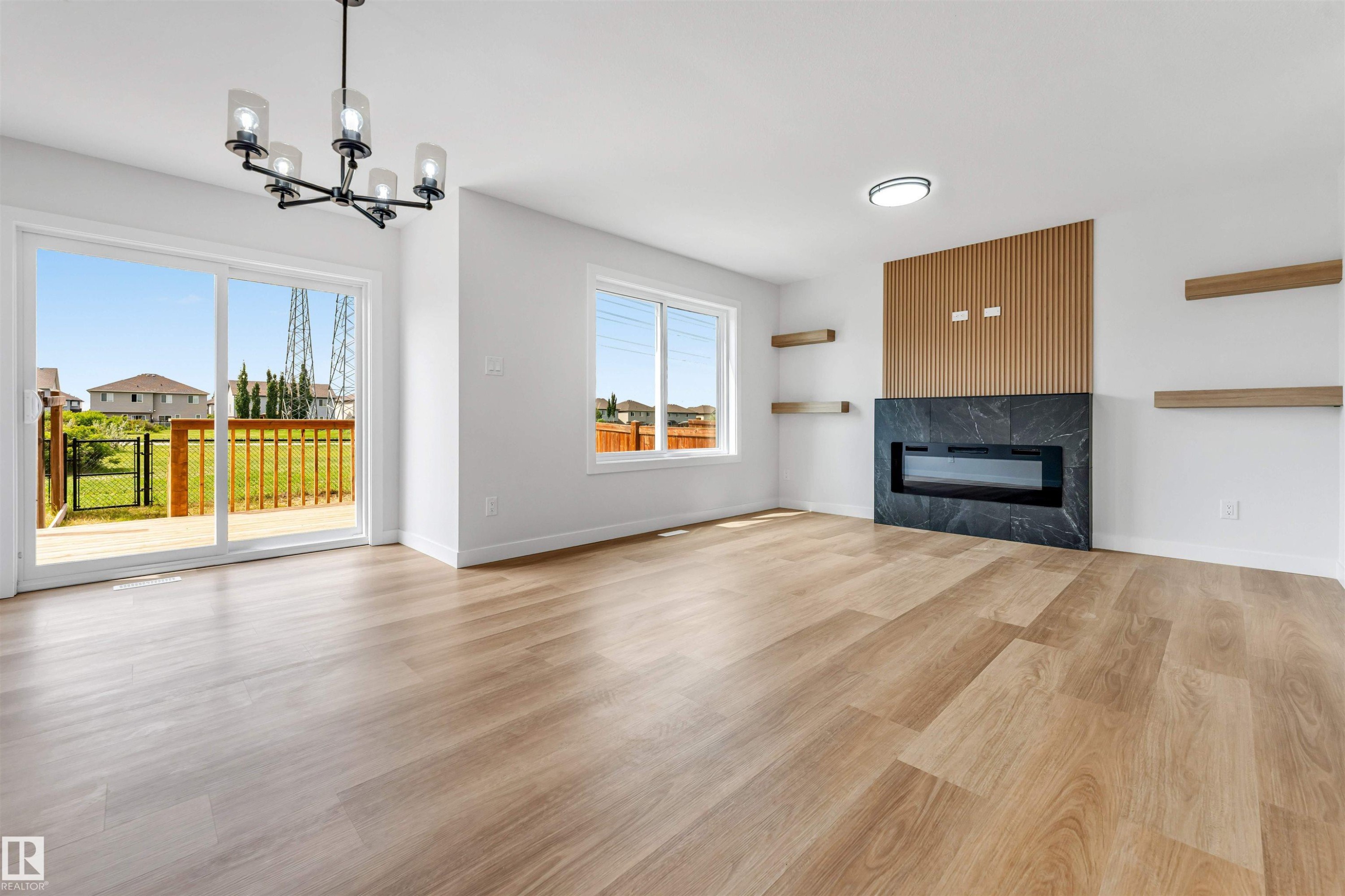Spacious living area featuring wood-finish flooring, a contemporary fireplace with dark stone surround, and an accent wall with vertical wood paneling - 1714 27 St. Nw, Edmonton, AB - Indoor Photo Showing Living Room With Fireplace