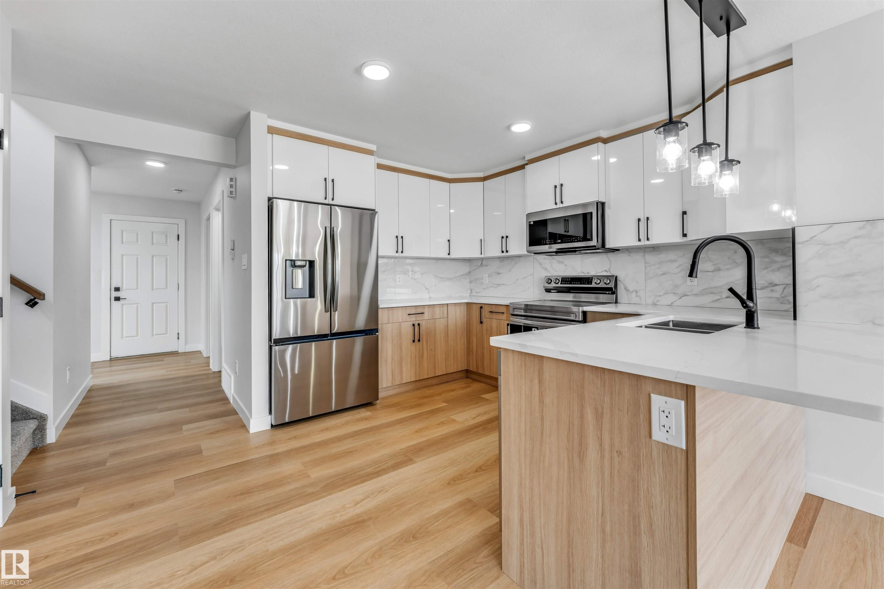 Modern kitchen featuring two-tone cabinetry, stainless steel appliances, a white countertop island, a matte black faucet, and a patterned backsplash - 1714 27 St. Nw, Edmonton, AB - Indoor Photo Showing Kitchen With Upgraded Kitchen