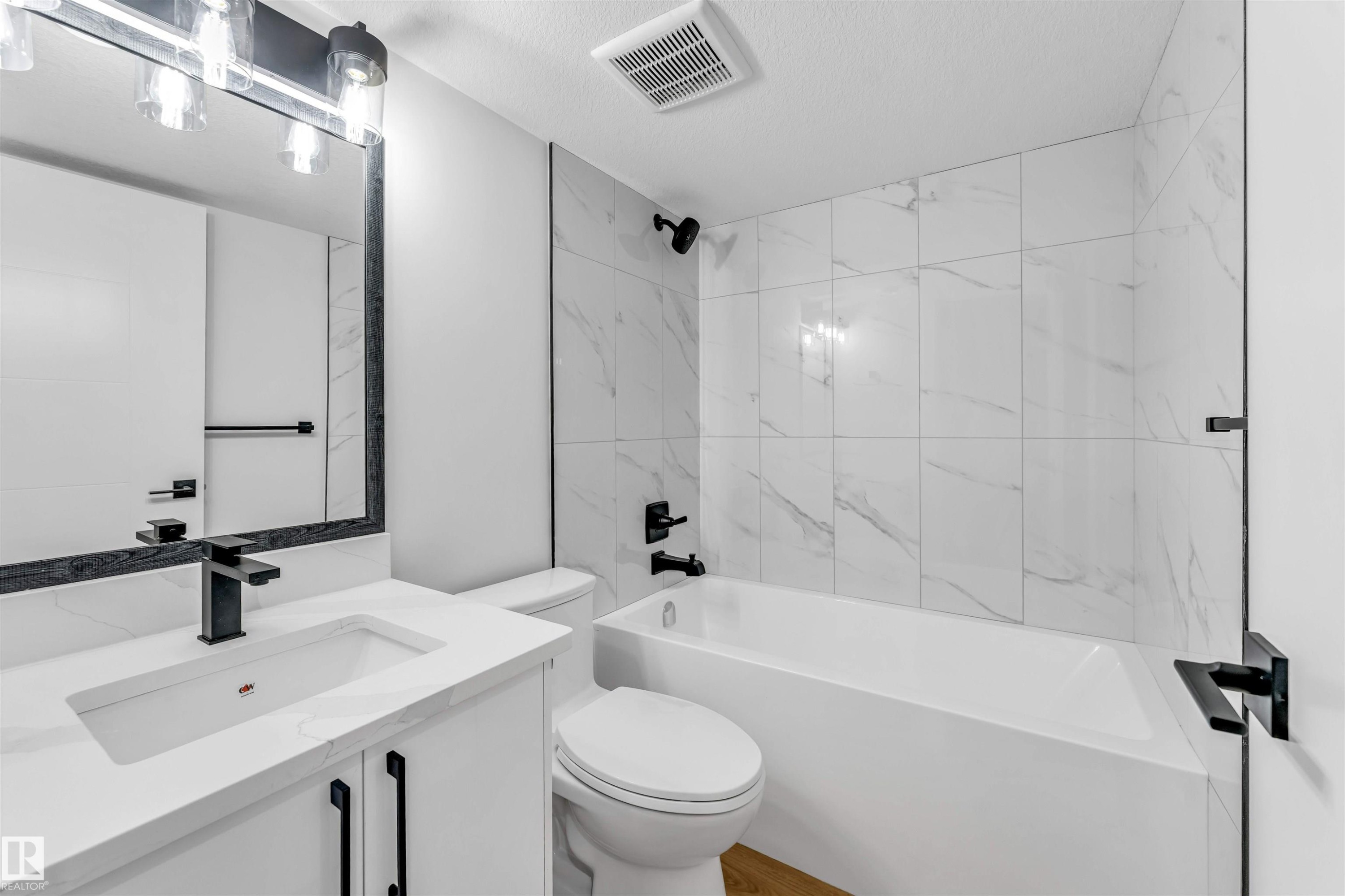 Bathroom featuring a white vanity with integrated sink, quartz countertop, and matte black fixtures - 1714 27 St. Nw, Edmonton, AB - Indoor Photo Showing Bathroom