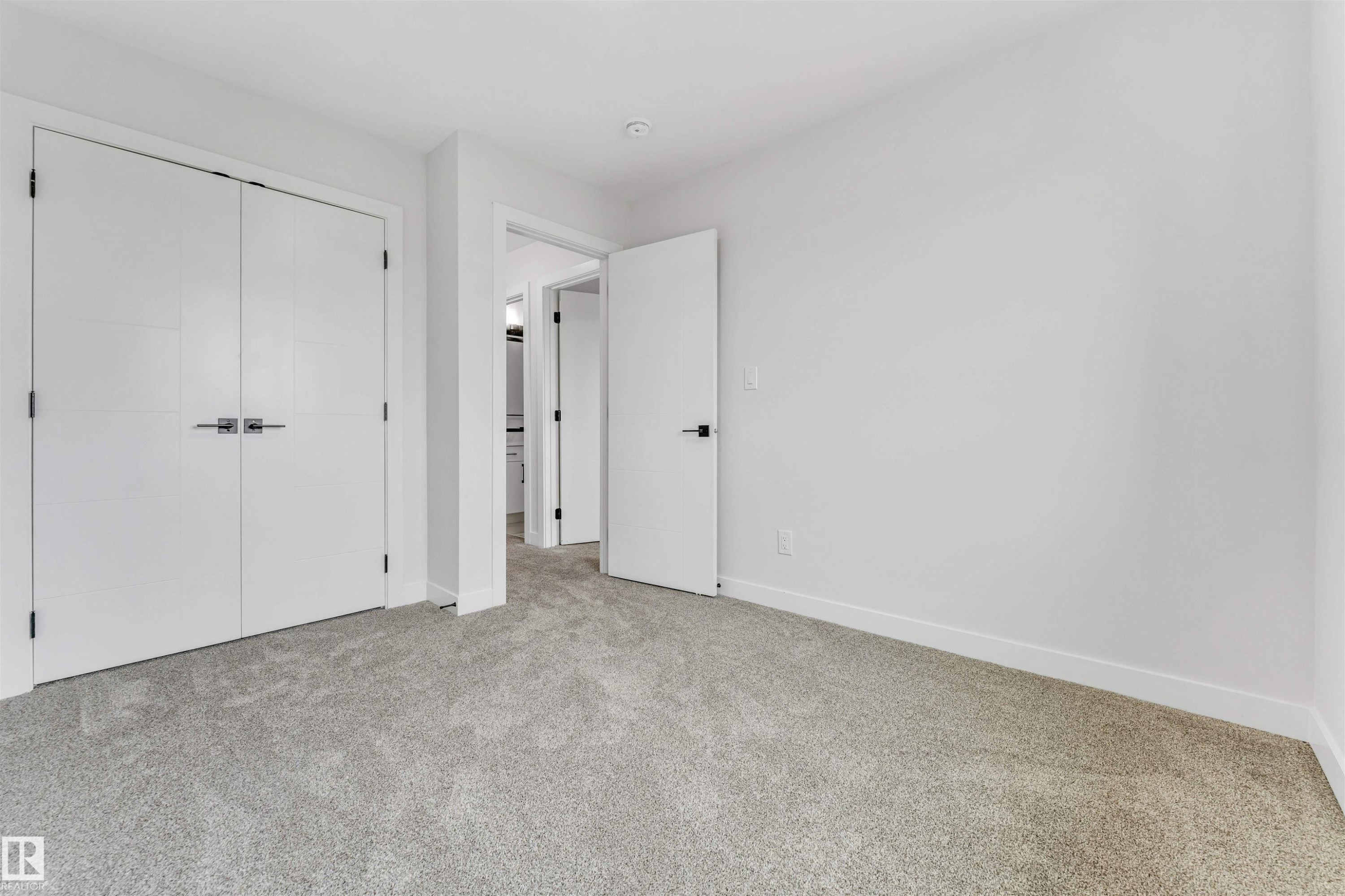 Bedroom featuring light gray carpet flooring, white walls, white baseboards, and a white double-door closet with dark hardware - 1714 27 St. Nw, Edmonton, AB - Indoor Photo Showing Other Room