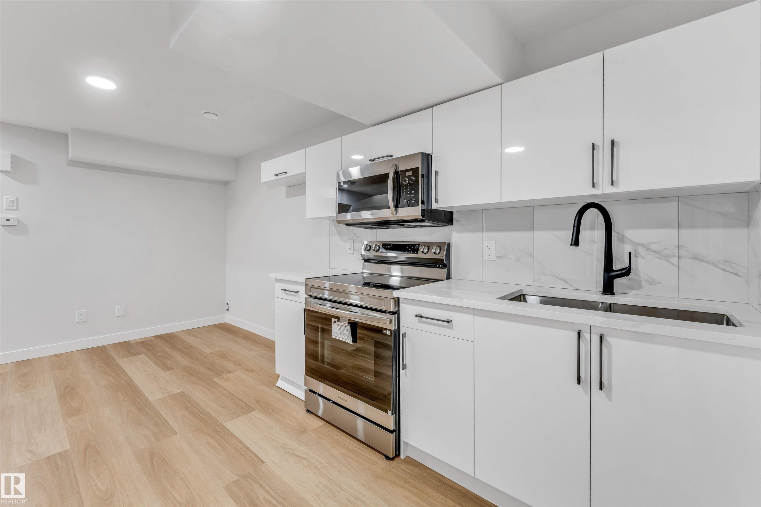Modern kitchen featuring white cabinetry, stainless steel appliances, a black gooseneck faucet, light wood-finish flooring, and recessed lighting - 1714 27 St. Nw, Edmonton, AB - Indoor Photo Showing Kitchen