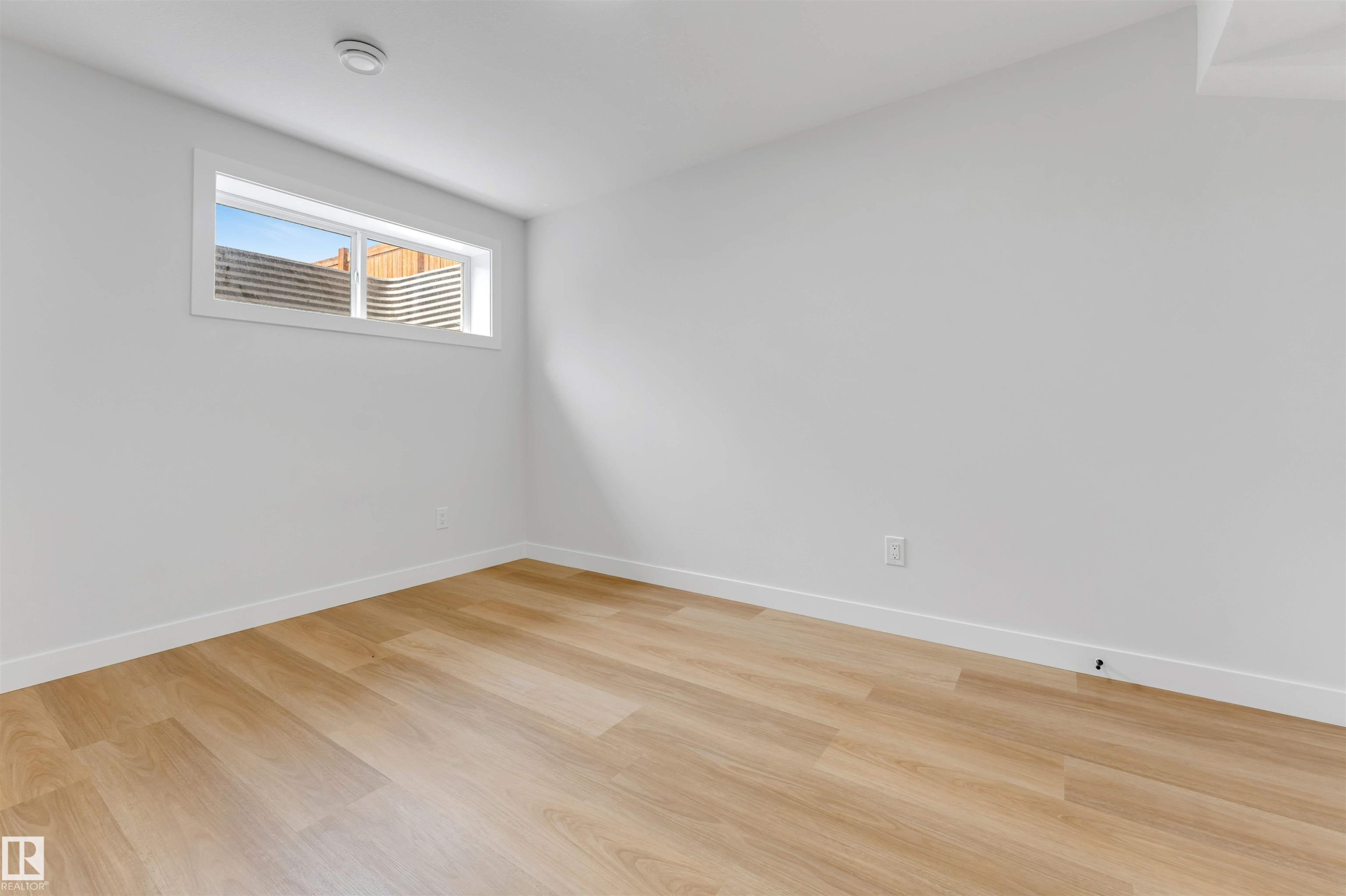 Light-filled room featuring wood-finish flooring, white baseboards, and a contemporary egress window - 1714 27 St. Nw, Edmonton, AB - Indoor Photo Showing Other Room