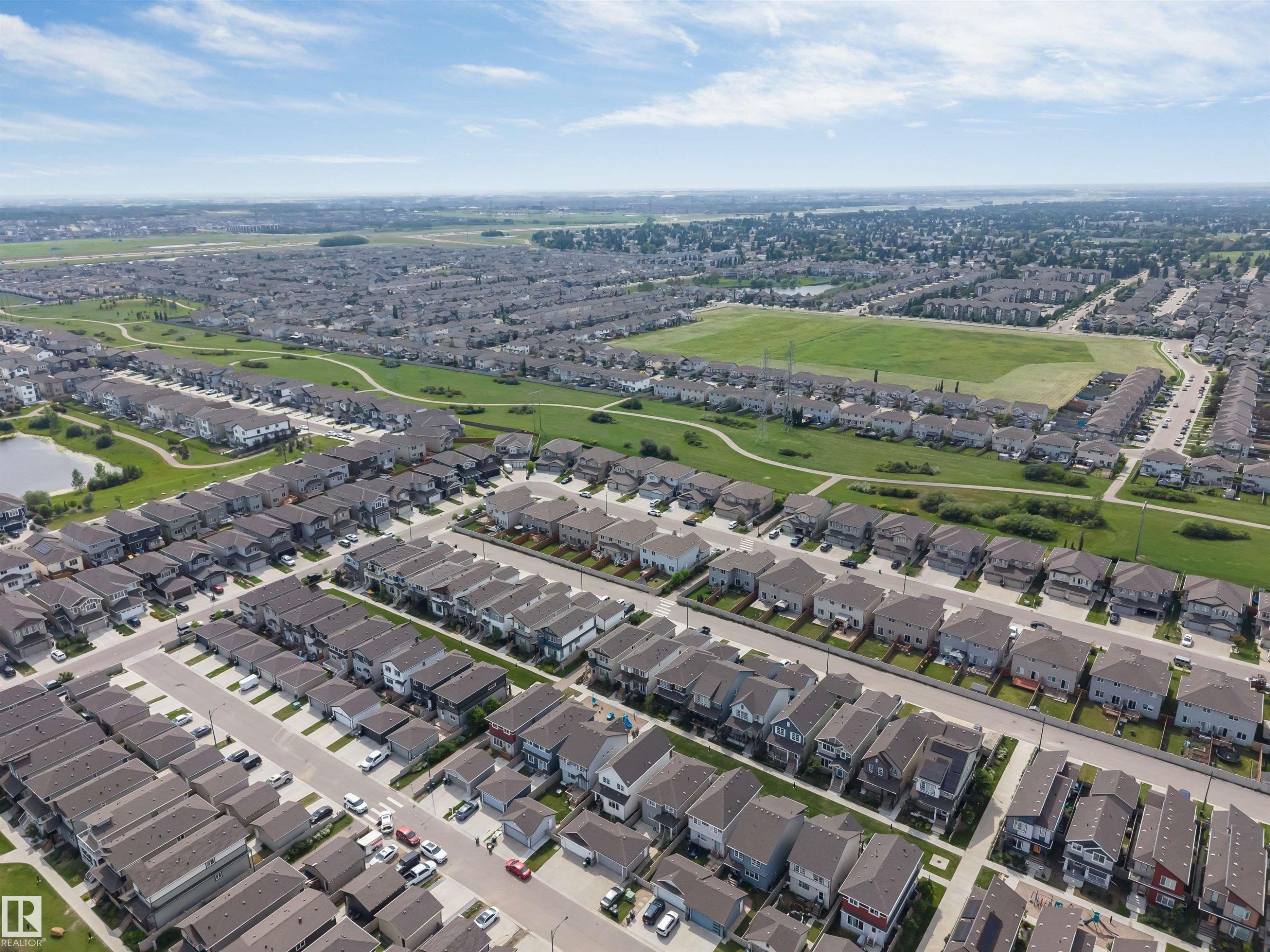 Aerial perspective of a developed residential area featuring a large green space, a community pond, and multiple streets with single-family homes - 1714 27 St. Nw, Edmonton, AB - Outdoor With View