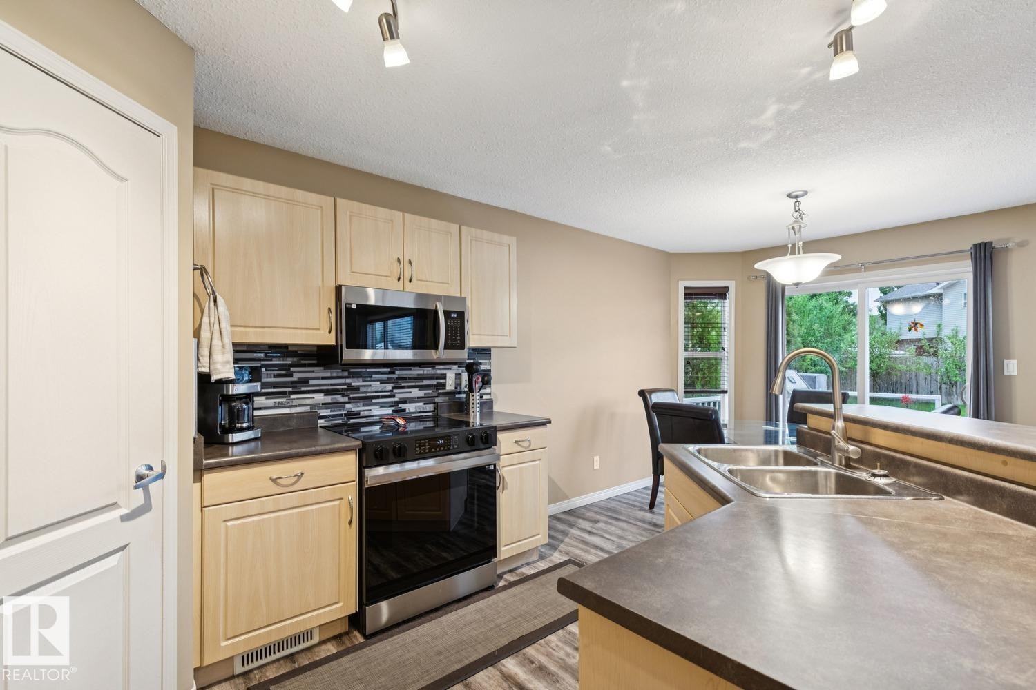 Kitchen featuring light wood cabinetry, dark countertops, and a full suite of stainless steel appliances - 16765 119 Street Nw, Edmonton, AB - Indoor Photo Showing Kitchen With Double Sink