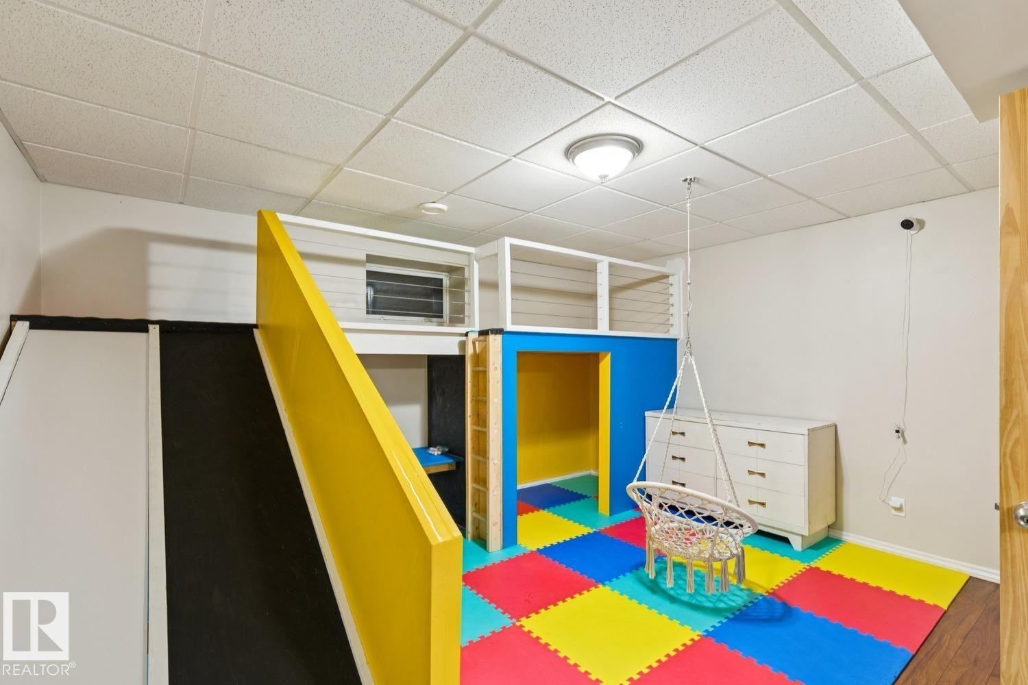 Recreational room featuring a multi-level loft structure with balustrade railing, a built-in slide, and a vibrant multi-colored floor mat - 16765 119 Street Nw, Edmonton, AB - Indoor Photo Showing Other Room