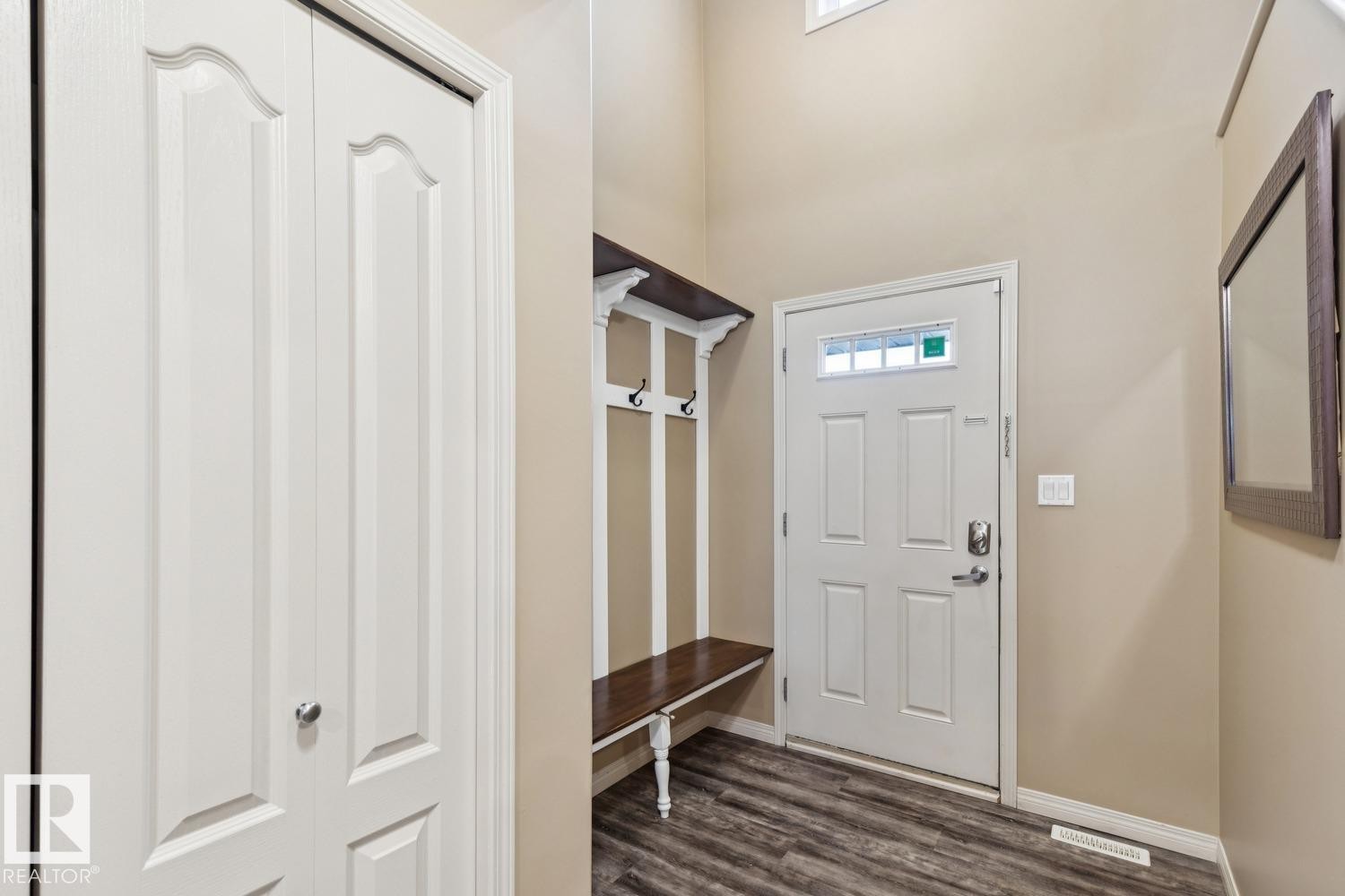 Entryway featuring wood-finish flooring, a built-in hall tree with bench and hooks, a white panel entry door with decorative glass, and a large wall-mounted mirror - 16765 119 Street Nw, Edmonton, AB - Indoor Photo Showing Other Room