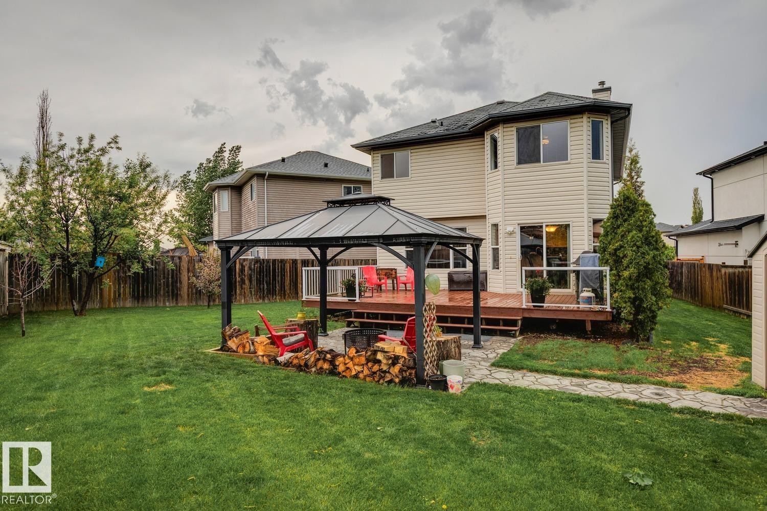 Spacious backyard featuring a large green lawn, a stone paver pathway, and a multi-level wooden deck with glass panel railing - 16765 119 Street Nw, Edmonton, AB - Outdoor With Deck Patio Veranda