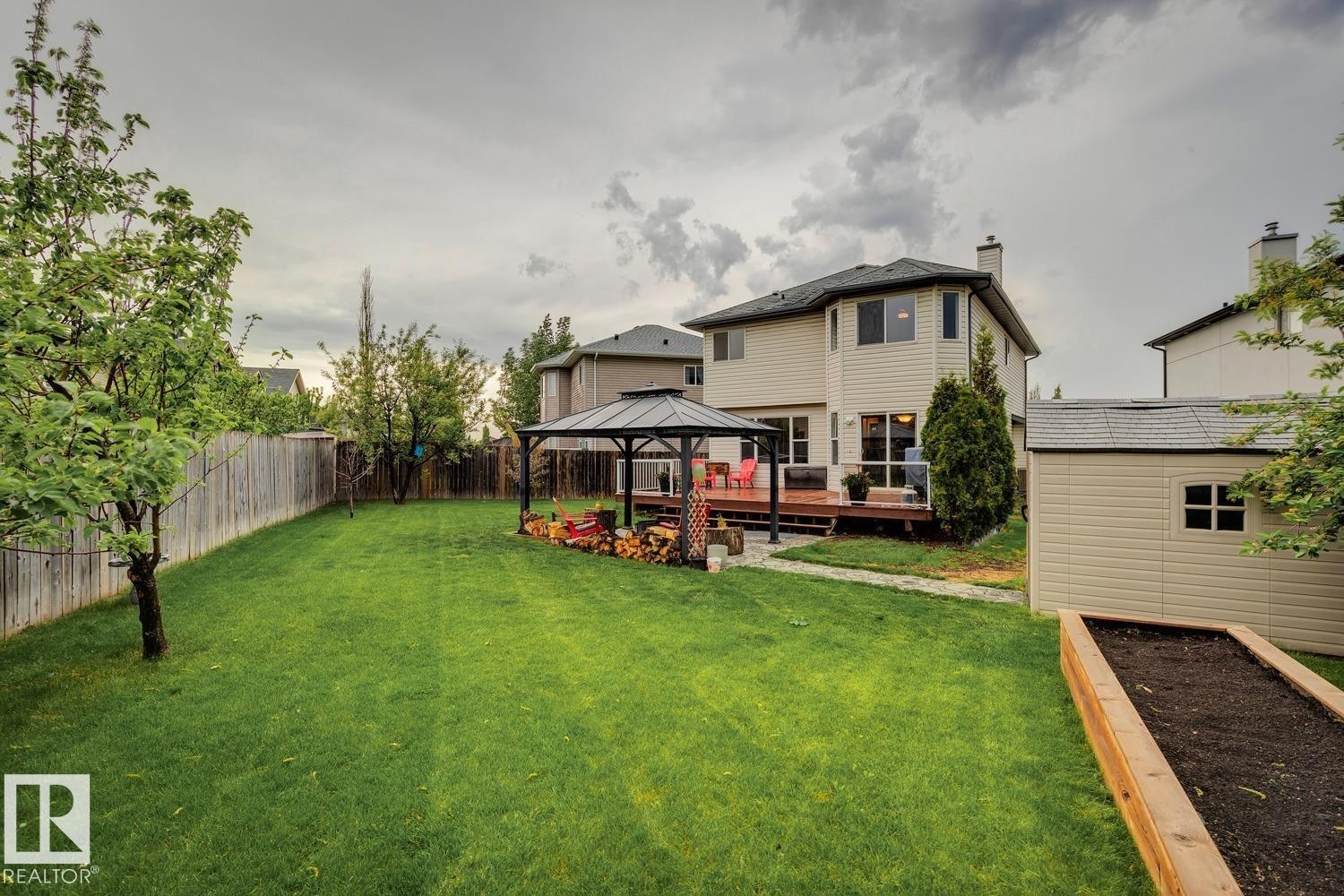Expansive backyard featuring a manicured lawn, a built-in wooden raised garden bed, a freestanding gazebo with a metal roof, a wooden privacy fence, and a detached storage shed - 16765 119 Street Nw, Edmonton, AB - Outdoor With Deck Patio Veranda
