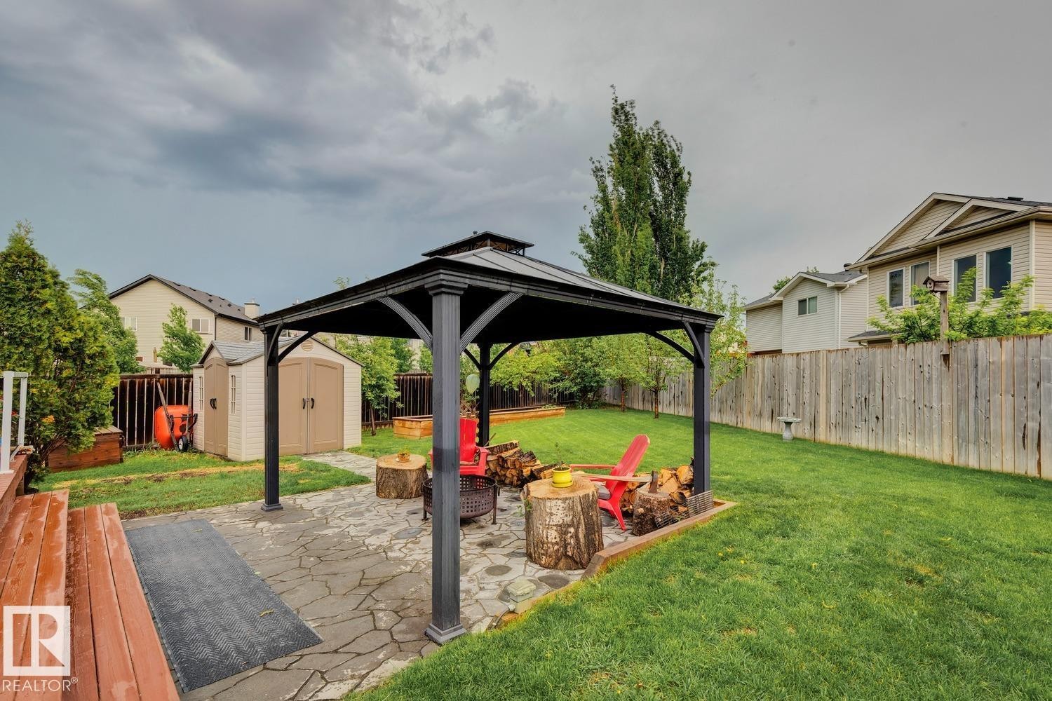 Expansive backyard featuring a stone patio with a metal gazebo, a manicured lawn, a privacy fence, and two storage sheds - 16765 119 Street Nw, Edmonton, AB - Outdoor