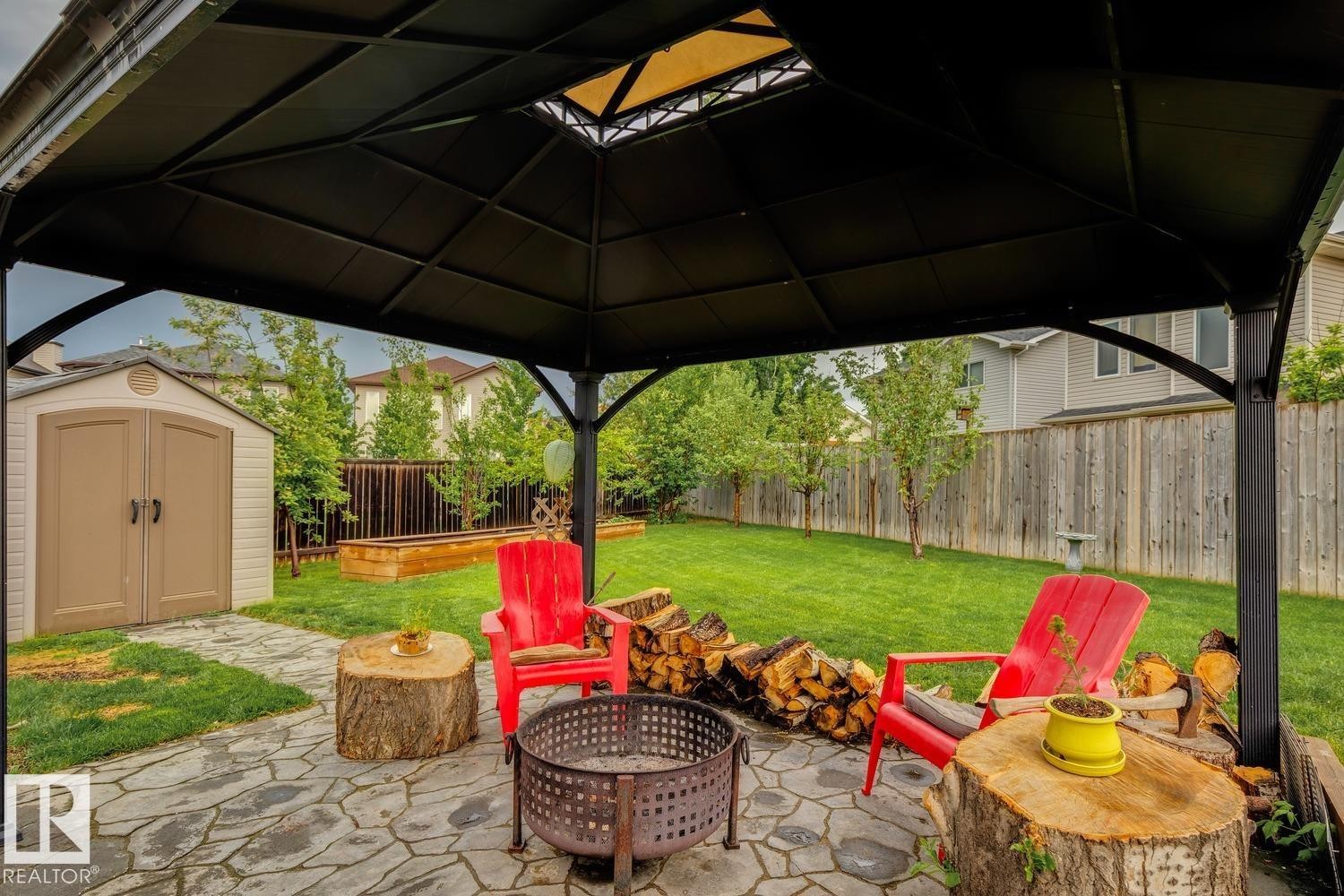 Stone patio beneath a black gazebo, featuring a fire pit - 16765 119 Street Nw, Edmonton, AB - Outdoor With Deck Patio Veranda