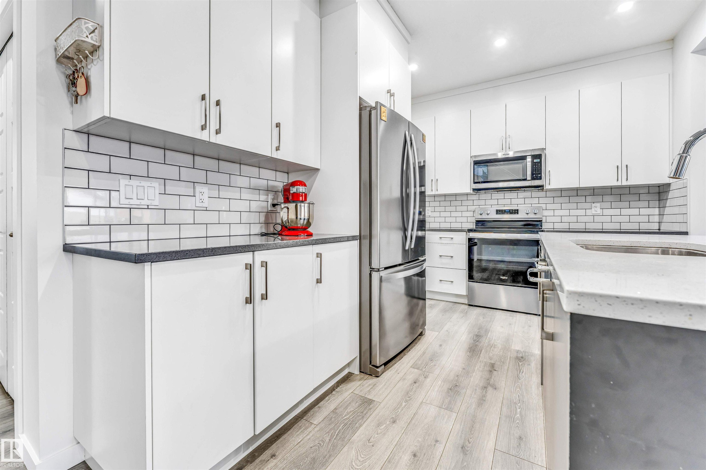 Modern kitchen featuring sleek white cabinetry, stainless steel appliances, subway tile backsplash, quartz countertops, and wood-finish flooring - 425 41 Street, Edmonton, AB - Indoor Photo Showing Kitchen With Stainless Steel Kitchen With Upgraded Kitchen