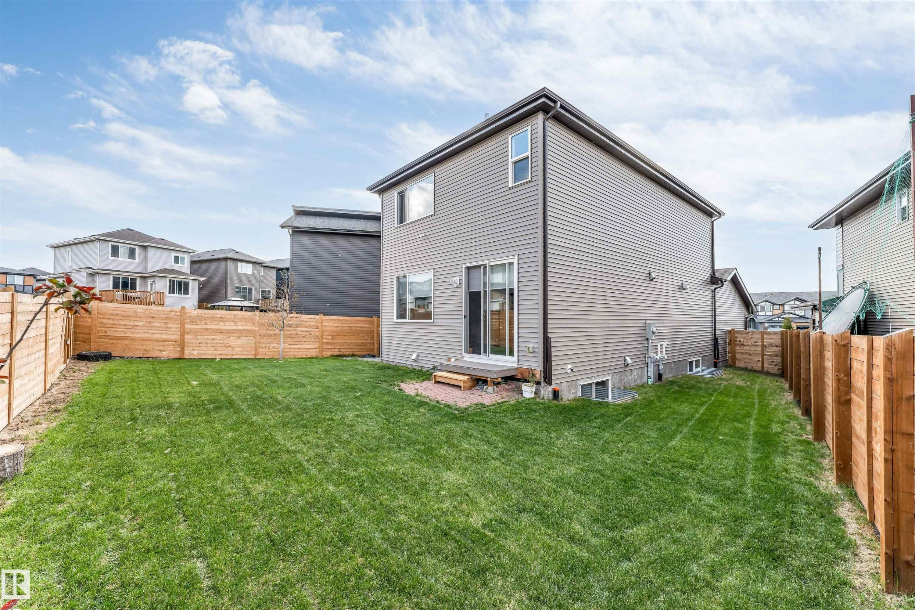 Expansive lawn area enclosed by a wooden privacy fence, featuring a ground-level patio with sliding glass doors - 425 41 Street, Edmonton, AB - Outdoor With Exterior