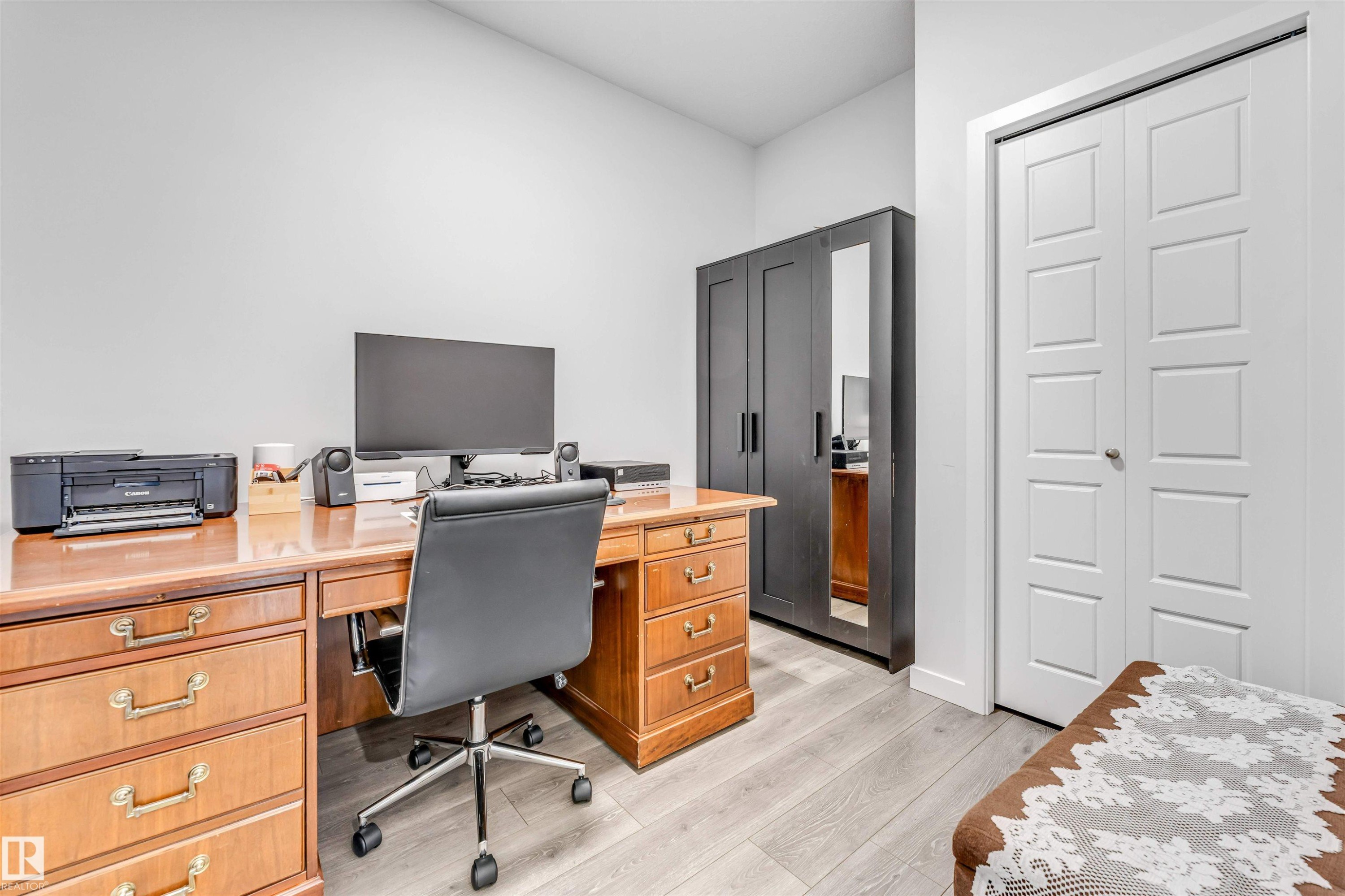 Light wood-finish flooring and neutral wall tones create a versatile space, featuring a built-in closet with paneled bifold doors and a dark wood-finish wardrobe with mirrored accents - 425 41 Street, Edmonton, AB - Indoor Photo Showing Office