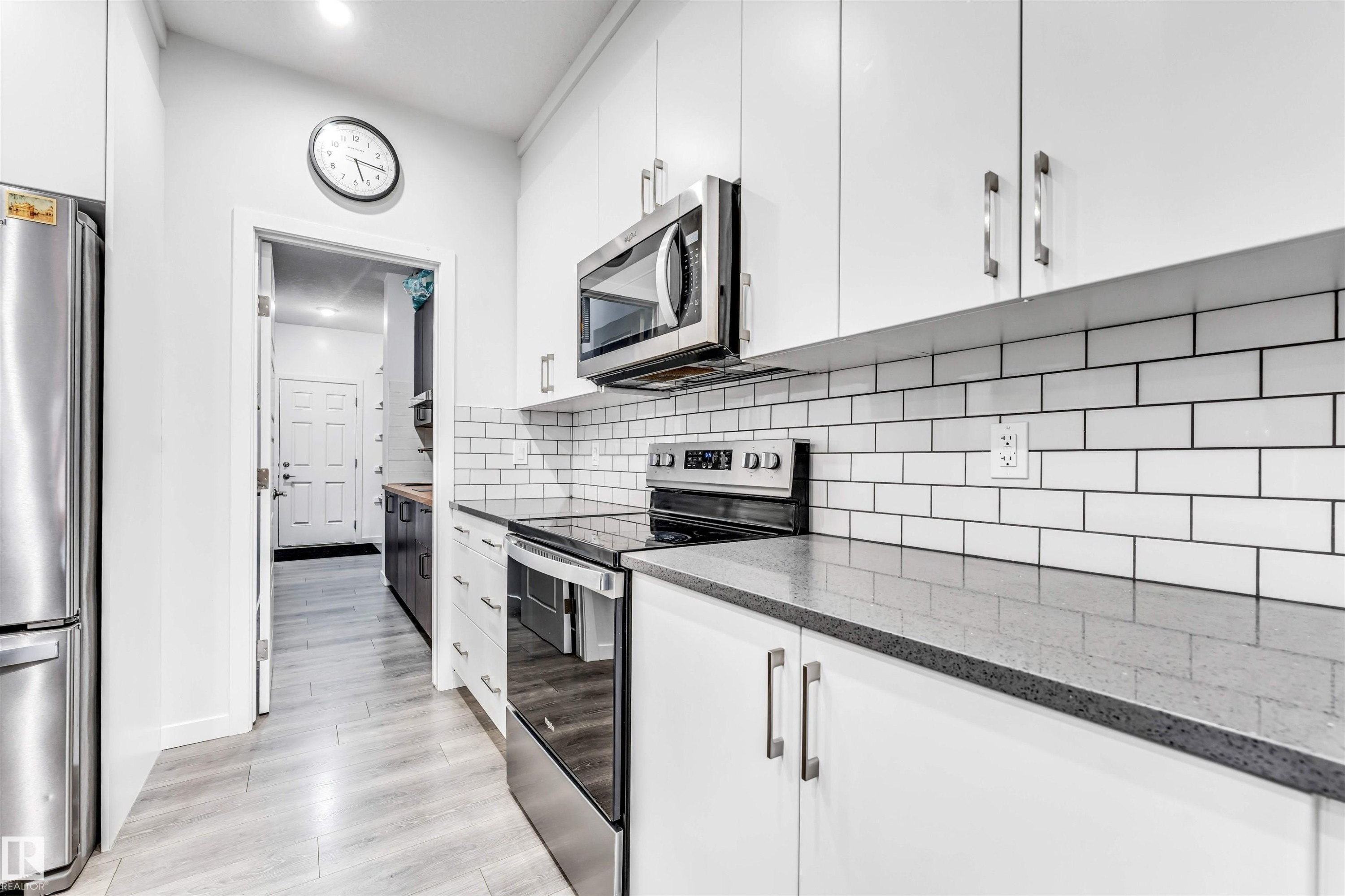 Modern kitchen featuring stainless steel appliances, crisp white cabinetry, a subway tile backsplash, light grey wood-finish flooring, and dark speckled countertops - 425 41 Street, Edmonton, AB - Indoor Photo Showing Kitchen With Stainless Steel Kitchen With Upgraded Kitchen