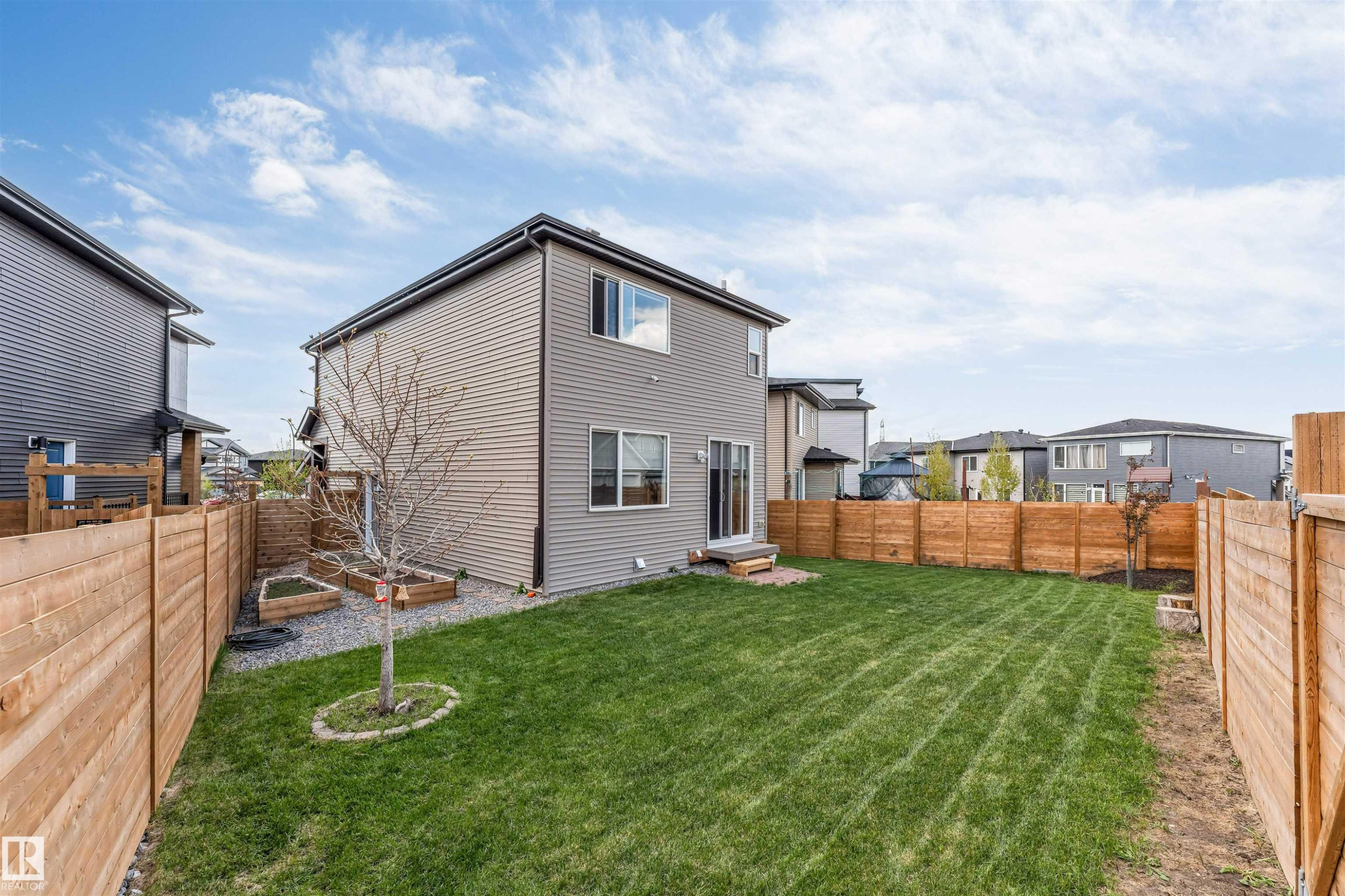 Expansive fenced backyard featuring a manicured lawn, established tree, and raised garden beds - 425 41 Street, Edmonton, AB - Outdoor