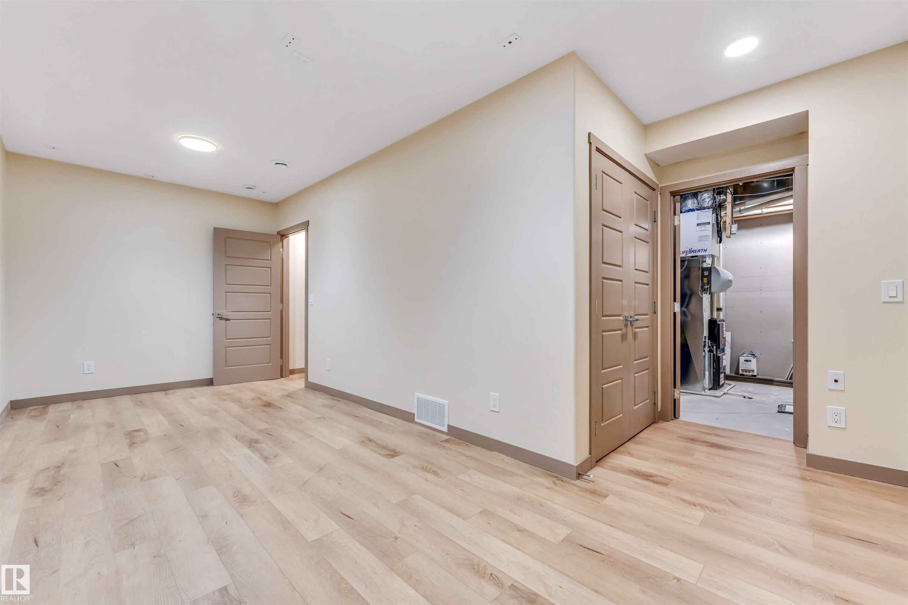 Spacious room featuring light wood-finish flooring, recessed lighting, neutral wall tones, and two paneled doors with brown trim - 425 41 Street, Edmonton, AB - Indoor Photo Showing Other Room