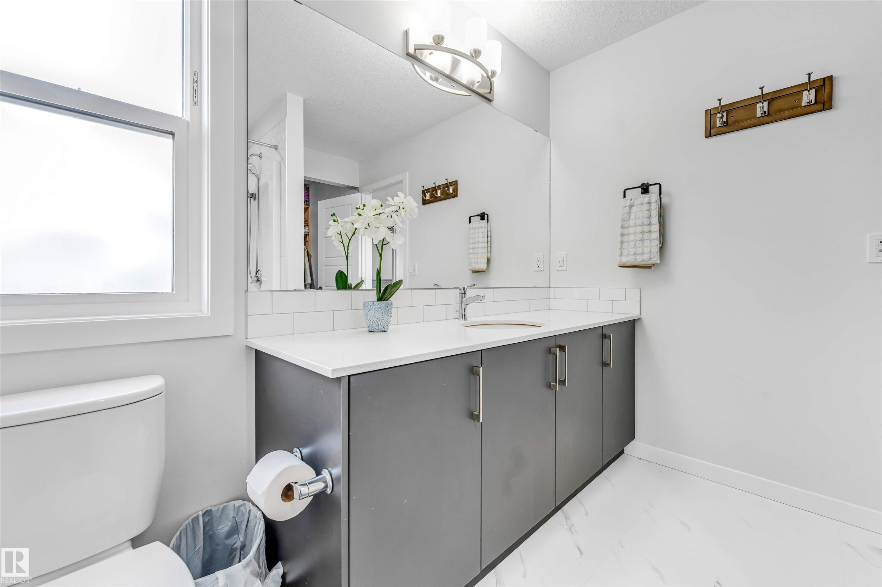 Bathroom featuring a single-pane window, a white toilet, a grey vanity with a white countertop, a rectangular mirror, and white subway tile backsplash - 425 41 Street, Edmonton, AB - Indoor Photo Showing Bathroom