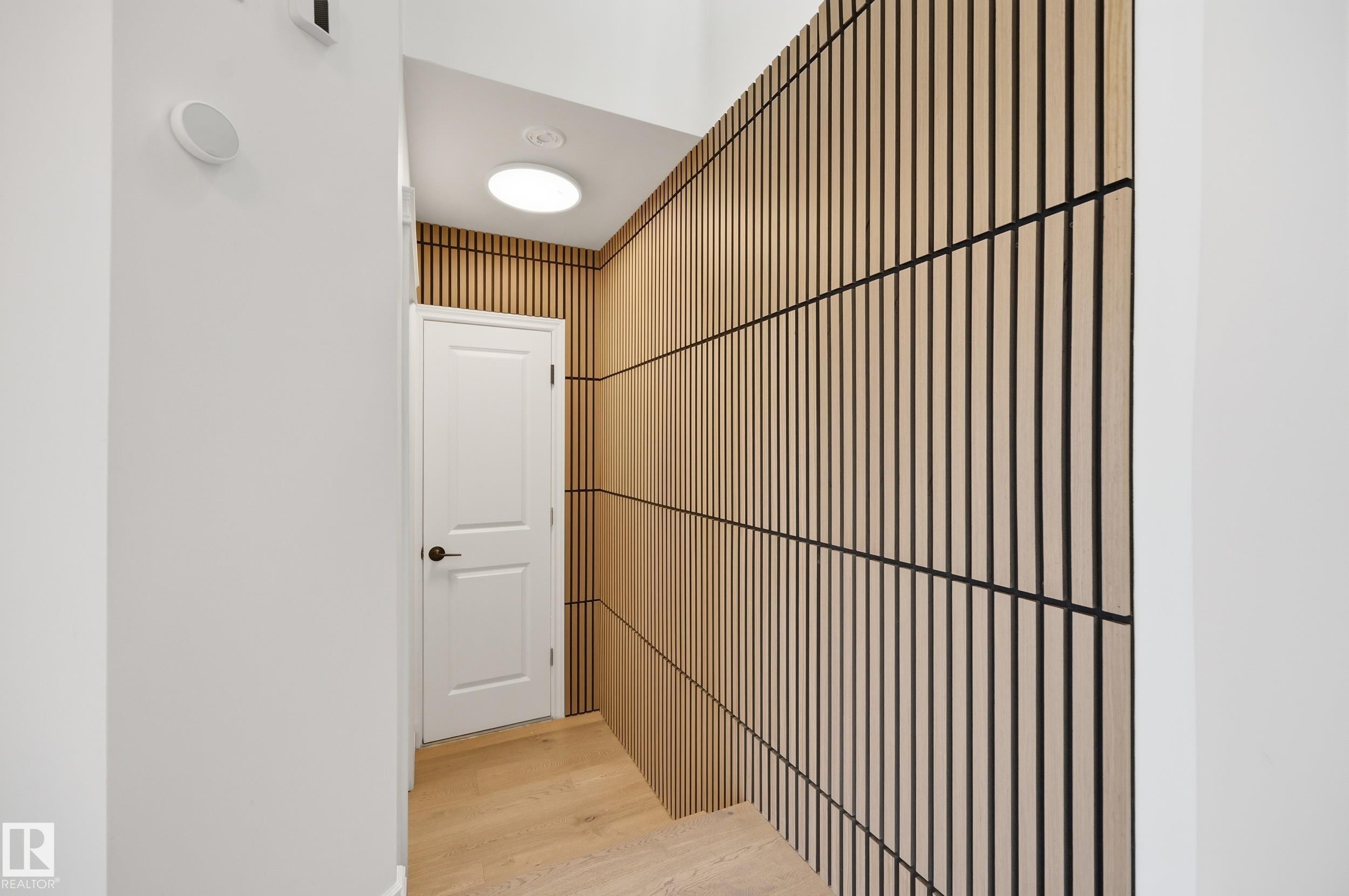 Modern hallway featuring a striking wood-slat accent wall, light wood-finish flooring, and crisp white painted walls - 1 Southfork Close, Leduc, AB - Indoor Photo Showing Other Room