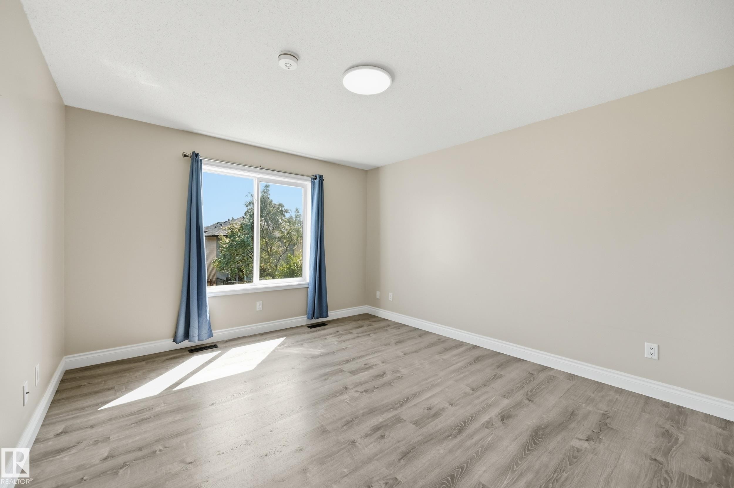Spacious room with wood-finish flooring, neutral-toned walls, a large window, and white trim - 1 Southfork Close, Leduc, AB - Indoor Photo Showing Other Room